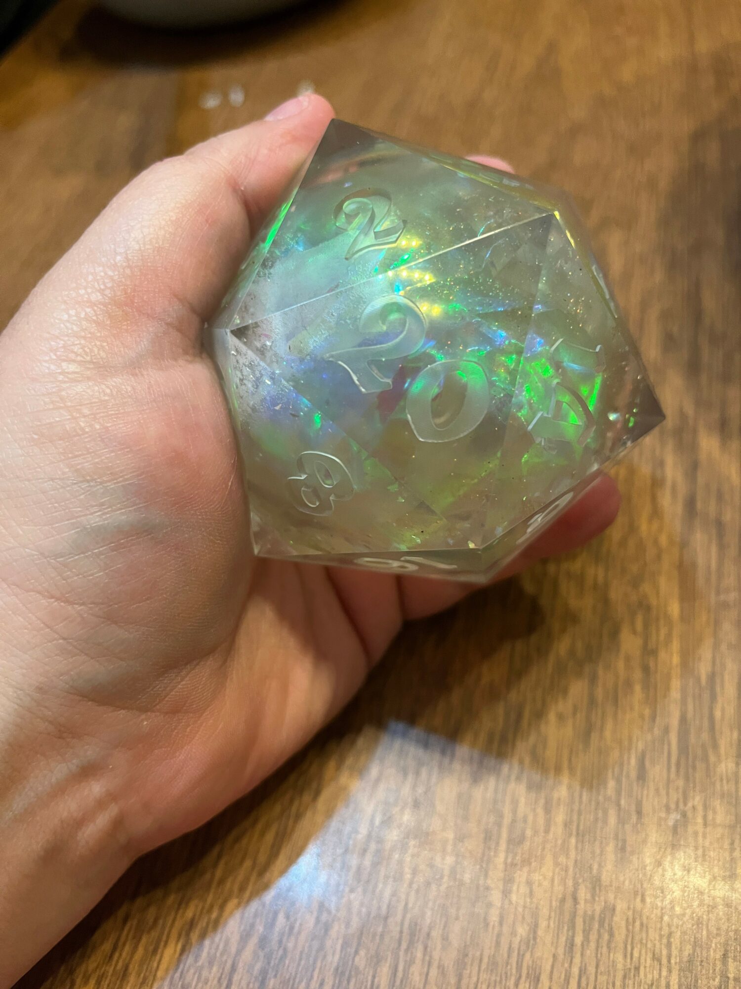 Hand holding a transparent, iridescent geometric object with swirling patterns, against a wooden surface background.