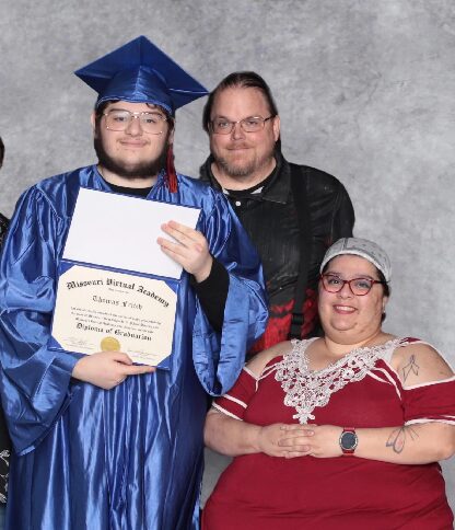 Young man in blue graduation gown and cap holding diploma, with two adults smiling beside him, against gray background.