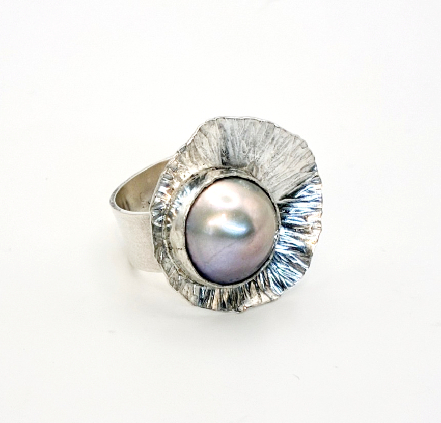 Ring with a large pearl surrounded by a textured metallic flower design, on a white background.
