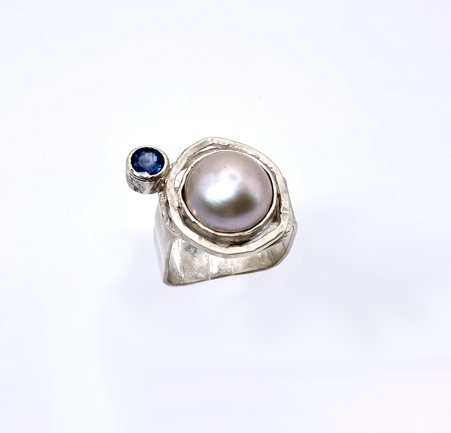Ring with a large pearl and a small blue gemstone on a white background.