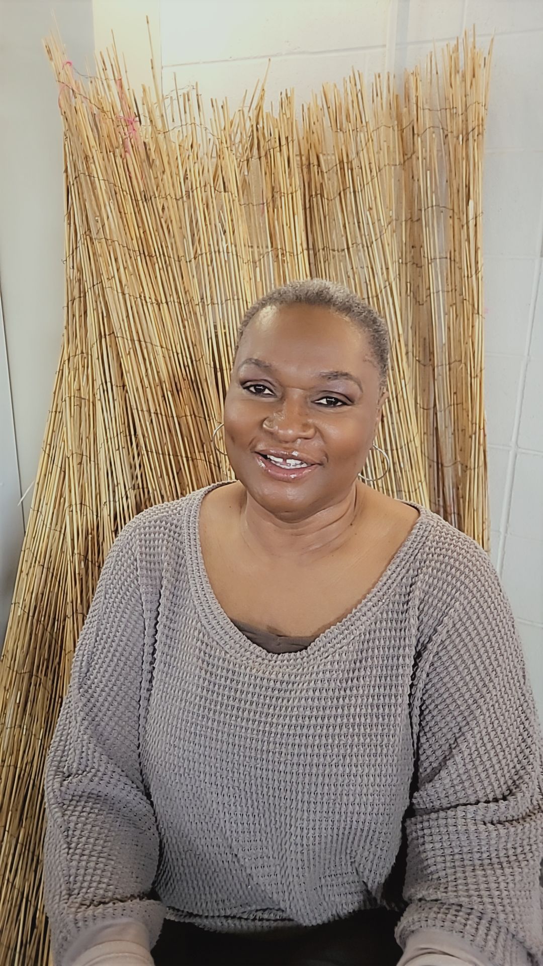 Smiling woman with short hair wearing a gray sweater, sitting in front of a bamboo backdrop.