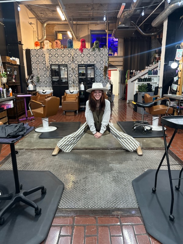 Person in striped pants and white hat stretching in a modern, stylish indoor space with chairs and decorative wall.