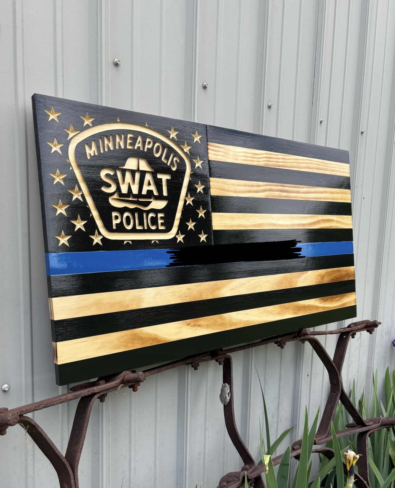 A black flag with gold and blue stripes, featuring a Minneapolis SWAT police badge and stars, mounted on a wall.
