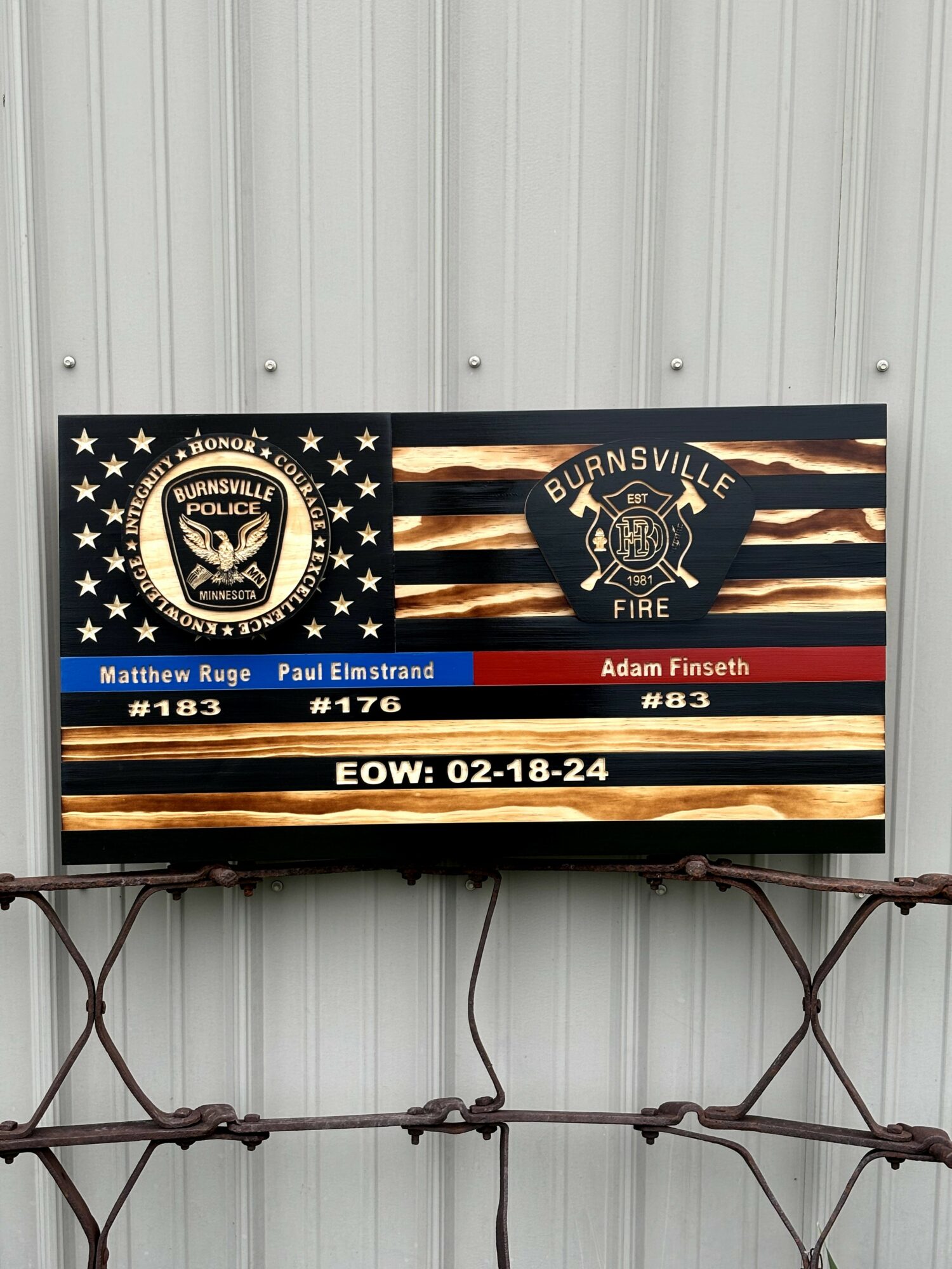 Display screen showing badges for Burnsville Police and Fire departments, with names and badge numbers, on a metal wall.