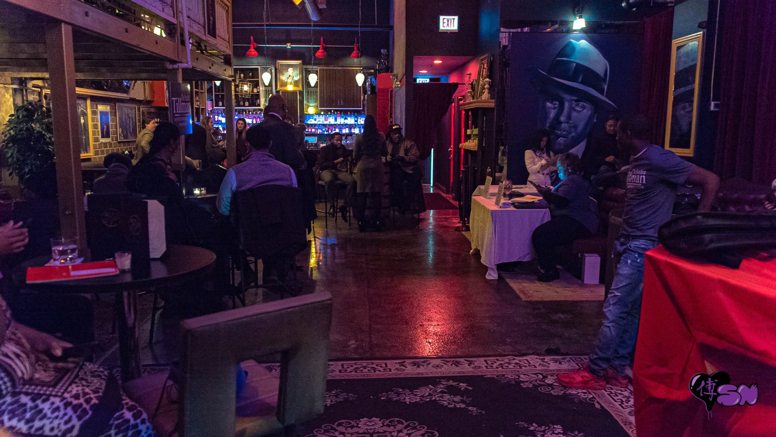 People sitting and standing in a dimly lit indoor venue with colorful lights and decorations.
