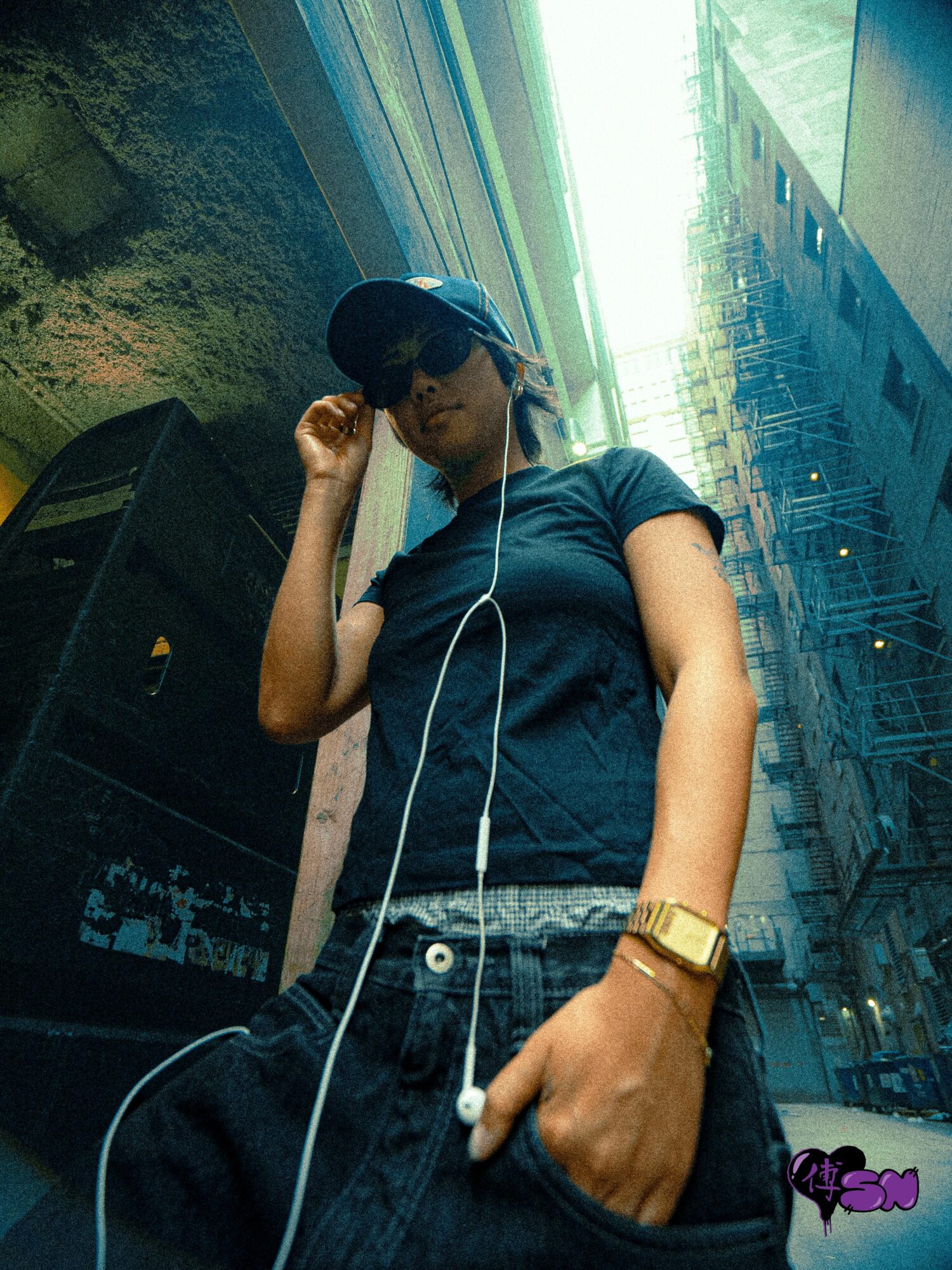 Young person wearing sunglasses, cap, and headphones, standing outdoors with tall buildings and glass reflections behind.