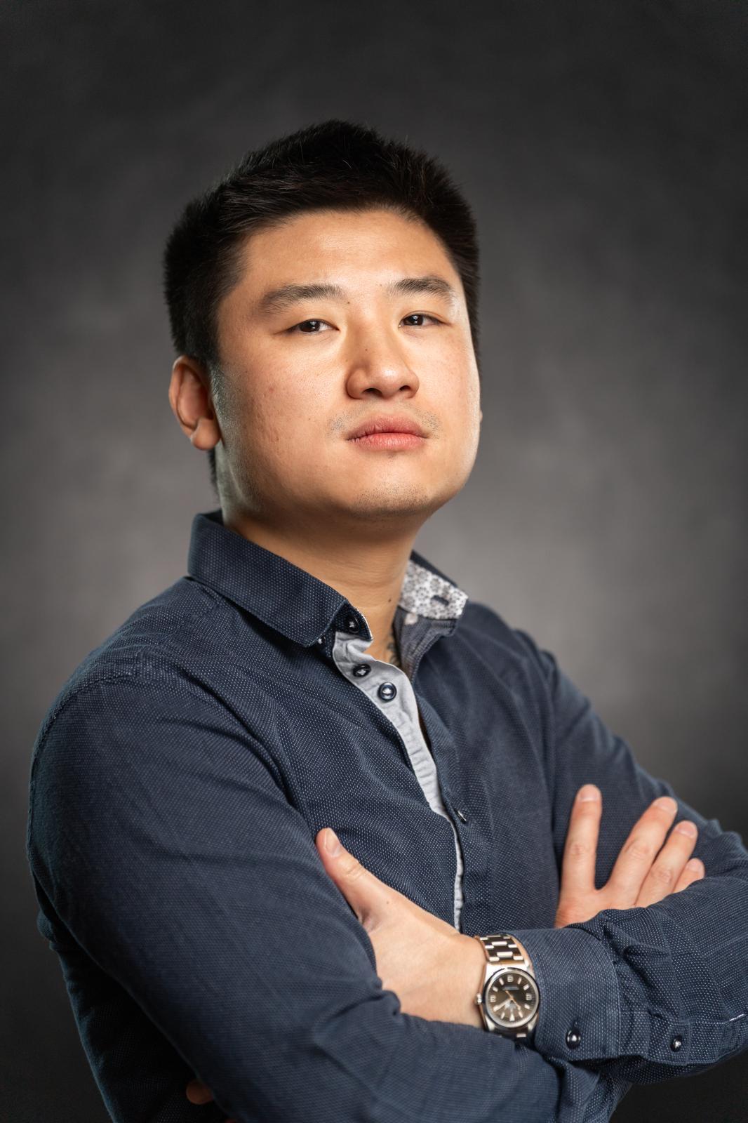 Young man with crossed arms, wearing a dark blue shirt, looking confidently at the camera, dark background.