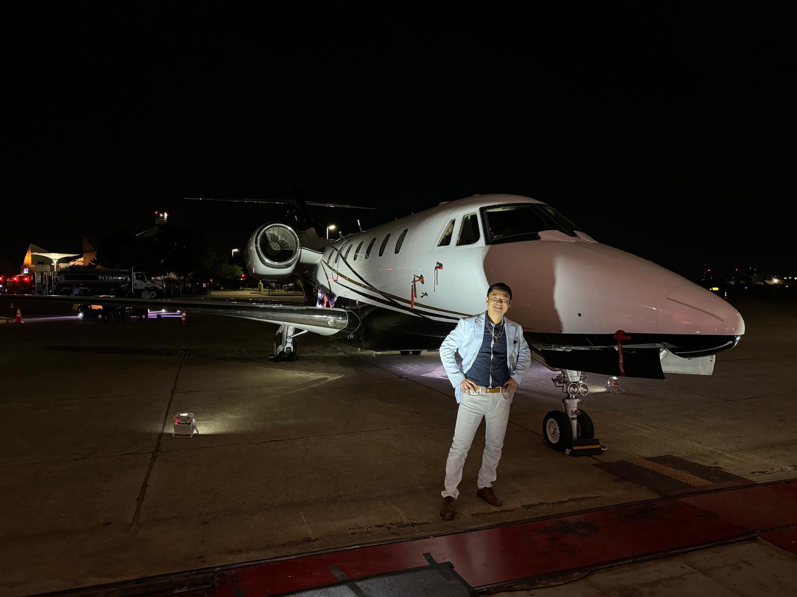 Person standing in front of a private jet at night, with airport tarmac visible.