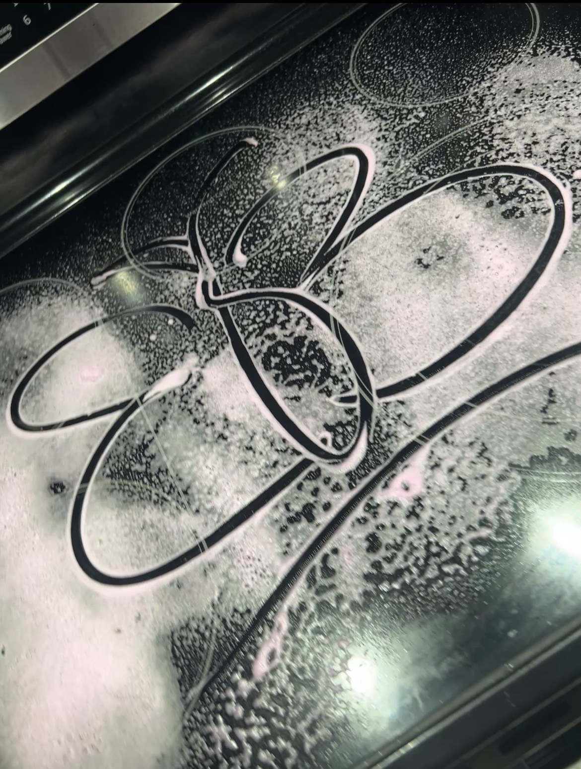 Spray-painted flower design on a black surface with white spray paint, featuring large petals and a central oval shape.