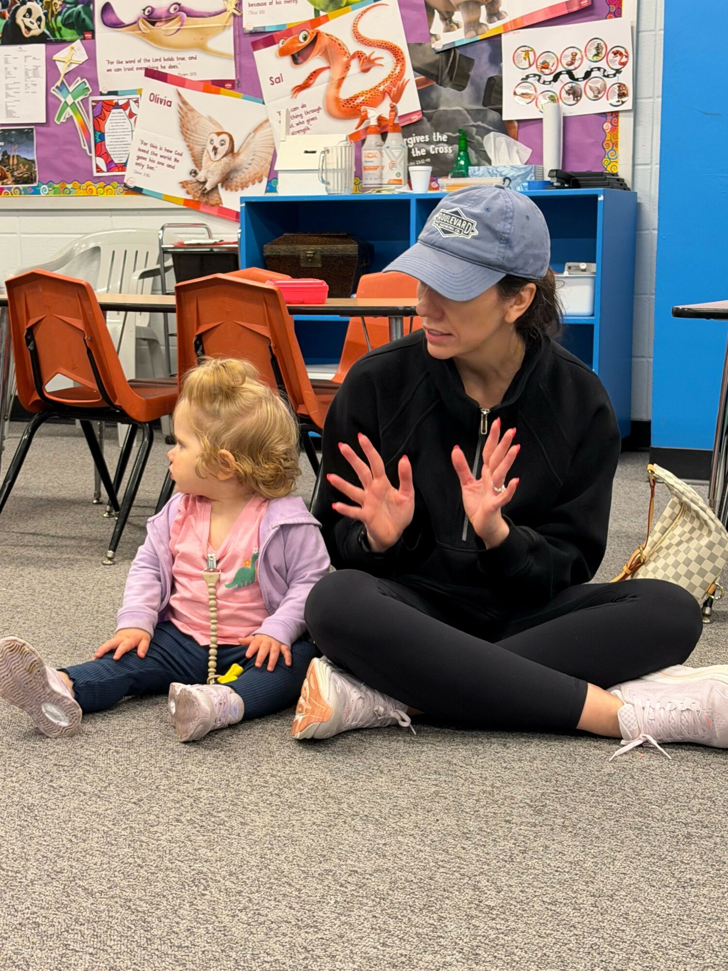 Adult and child sitting on the floor, engaging in conversation, with colorful posters and shelves in the background.