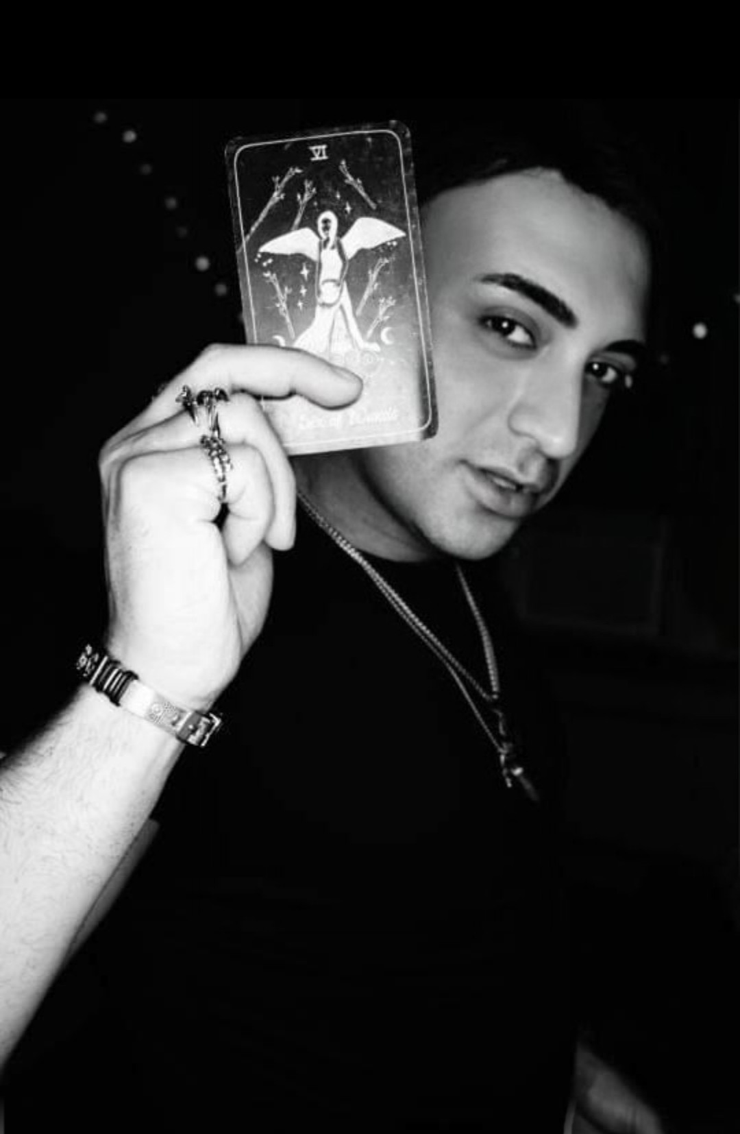 Woman holding a phone with a tarot card image, looking at the camera, in black and white.