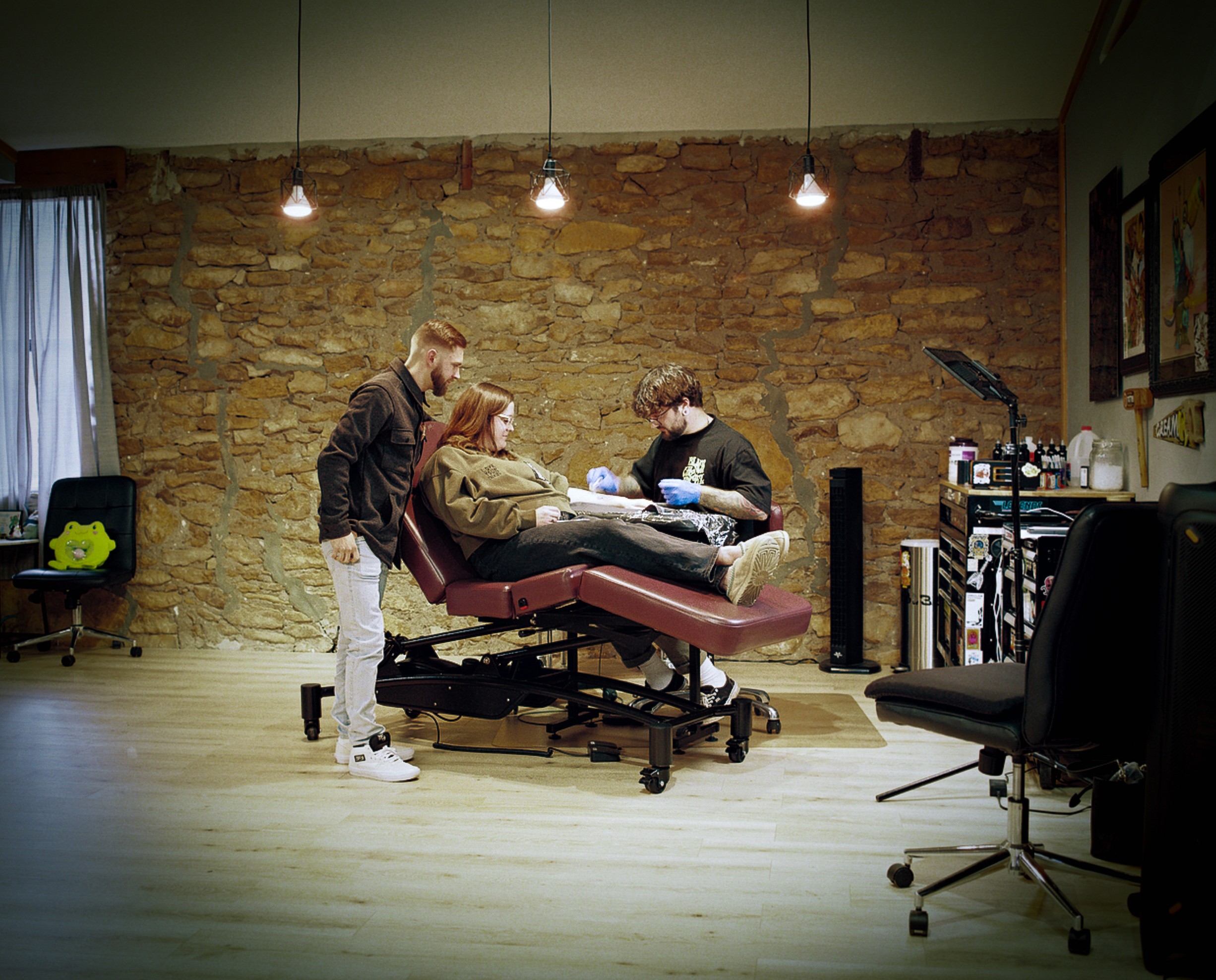 Three people in a room with a brick wall, one person lying on a medical examination table, two others attending to them.