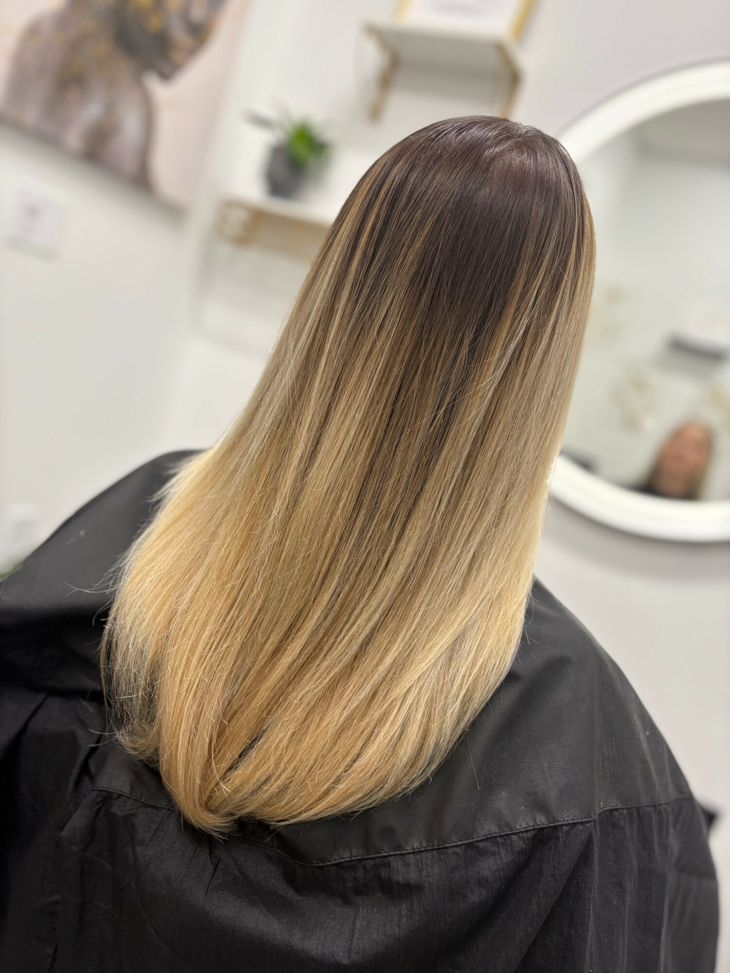 Back of a person's head with long, straight, ombre hair from dark brown to blonde, in a salon setting