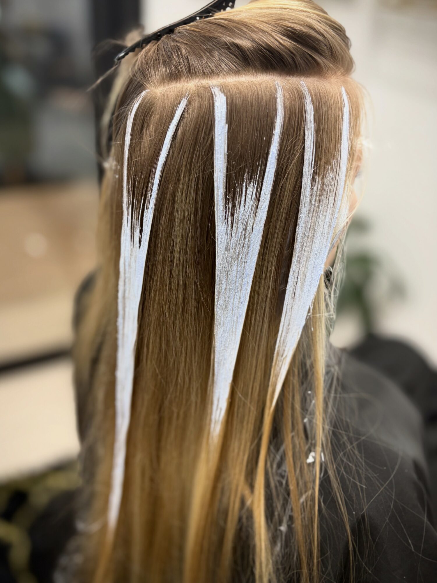 Person with blonde hair having white streaks applied in a salon, viewed from the back.