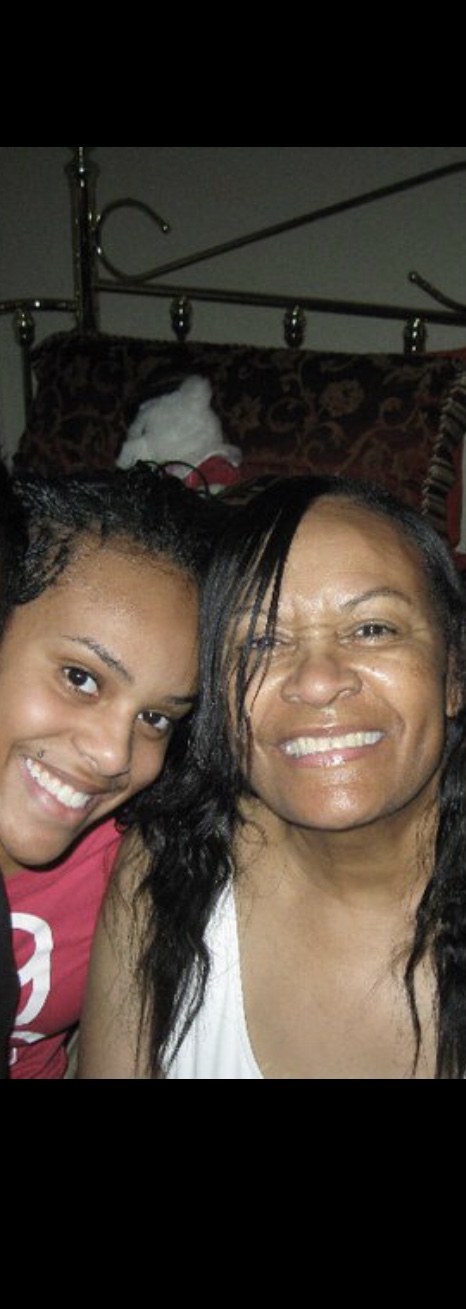 Two women smiling closely, one with curly hair and the other with straight hair, in a dimly lit room.