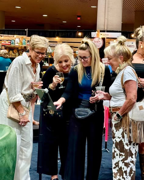 Four women are gathered together, smiling and holding drinks in a store or mall setting.