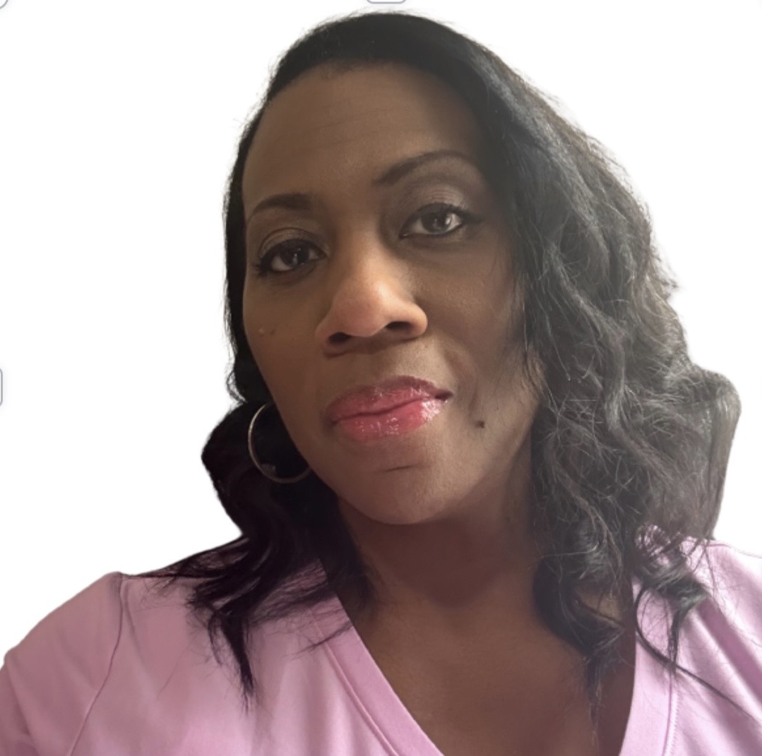 Woman with dark hair styled in loose waves, wearing a pink top, looking at the camera with a neutral expression.