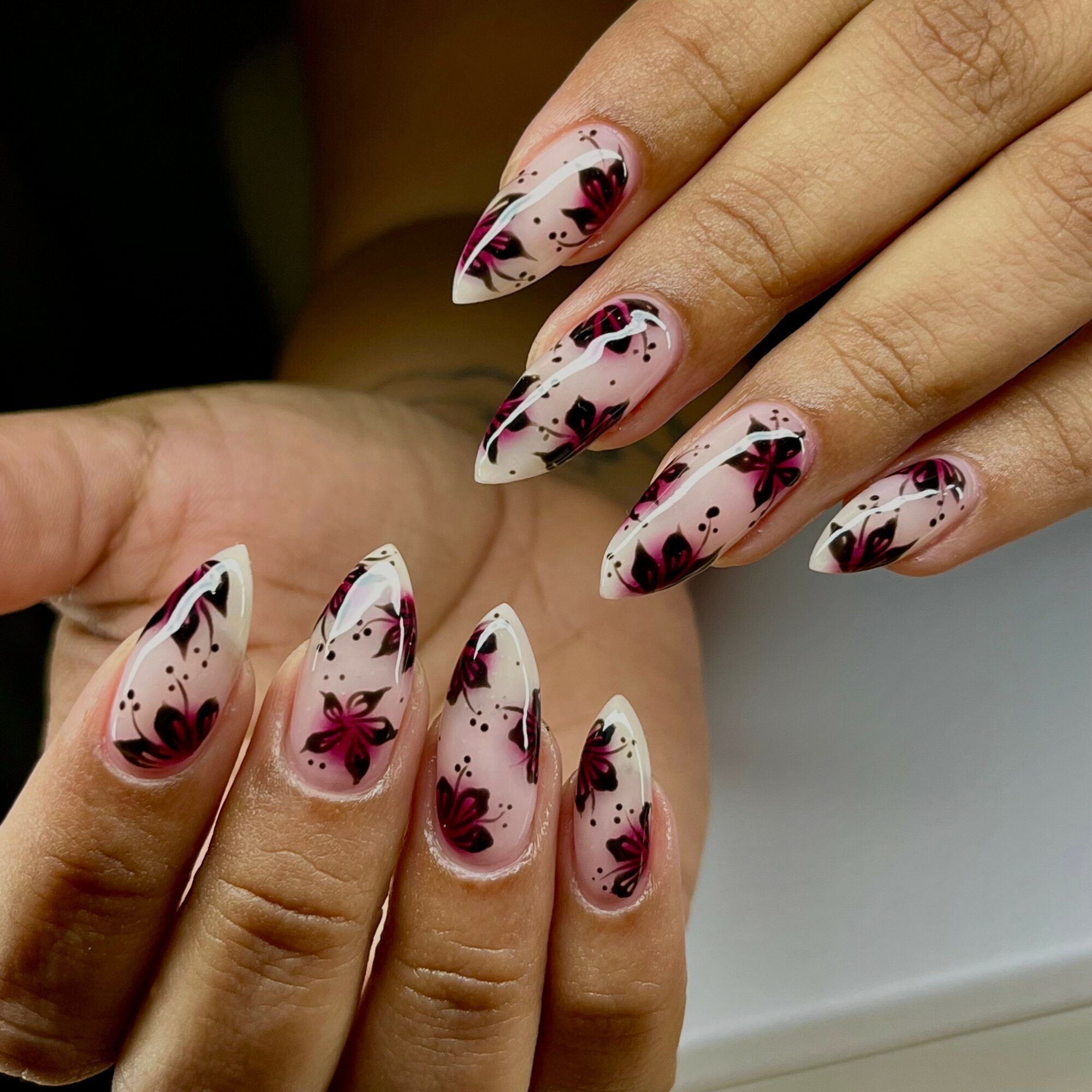 Close-up of hands with decorated nails featuring pink, black, and white floral and abstract designs.