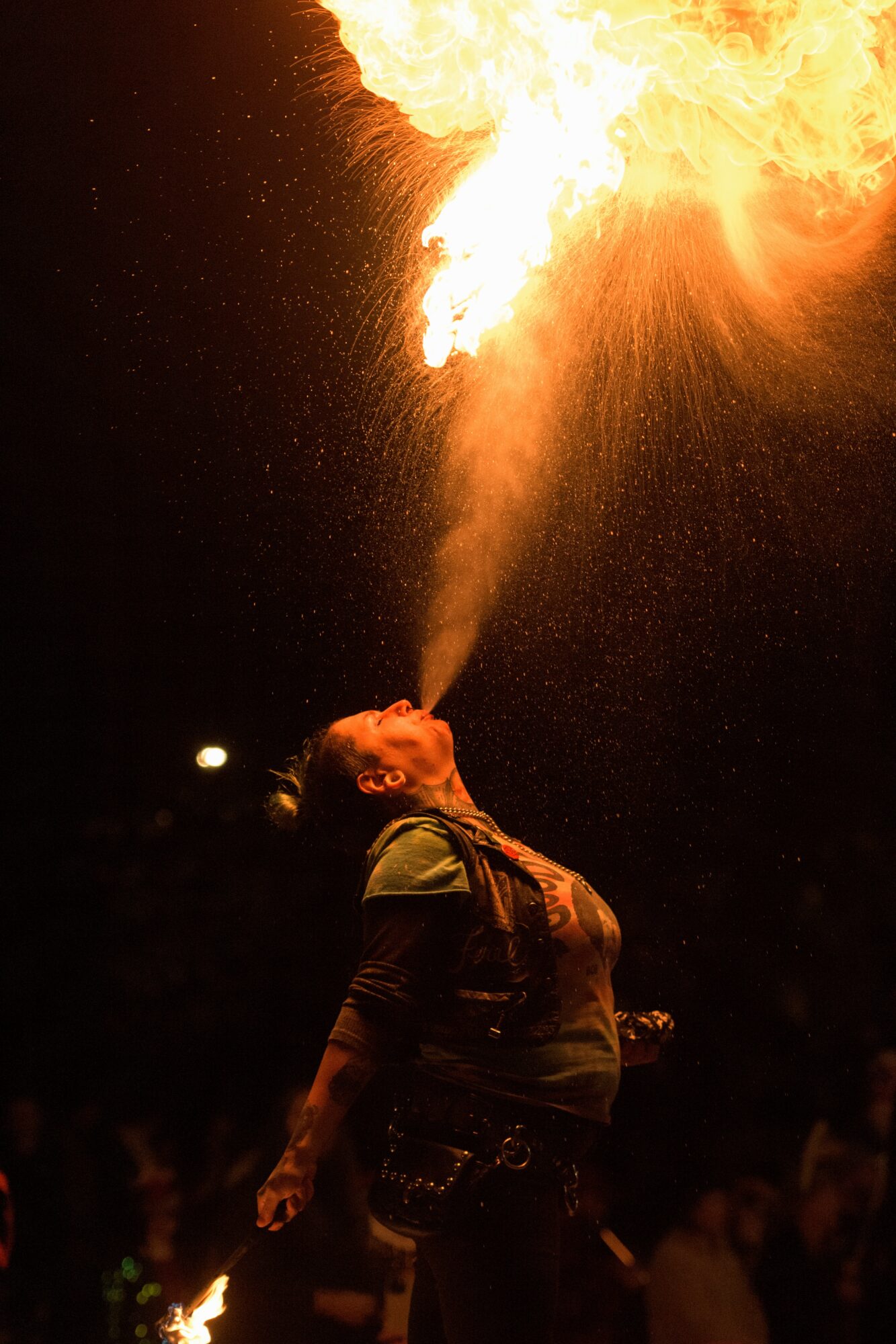 Person performing fire breathing, expelling a large flame into the air at night.