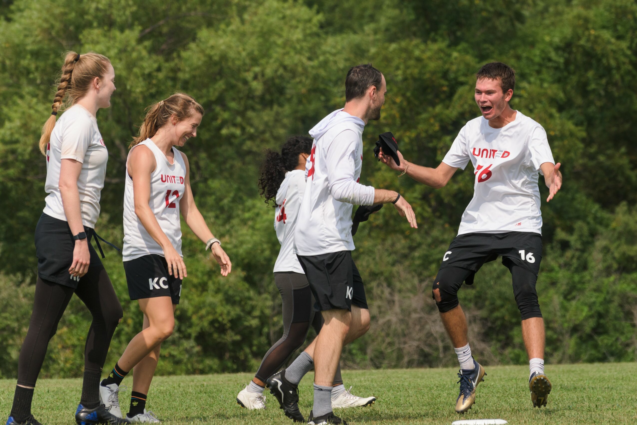 Group of people celebrating outdoors on grass, some jumping and smiling, with trees in the background.