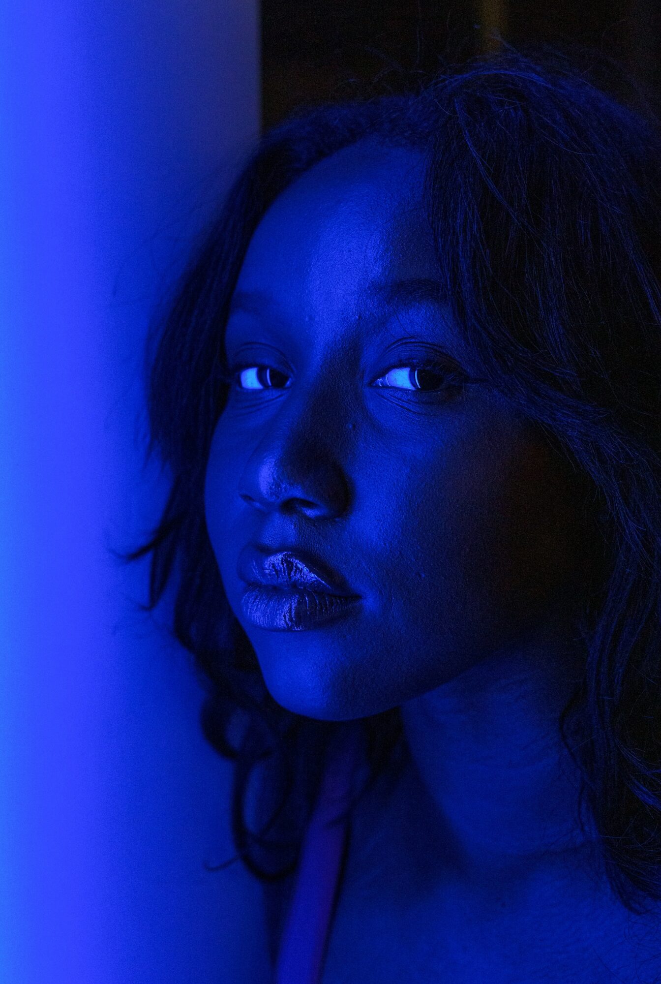 Close-up of a woman's face illuminated by blue light, with dark hair and a serious expression.