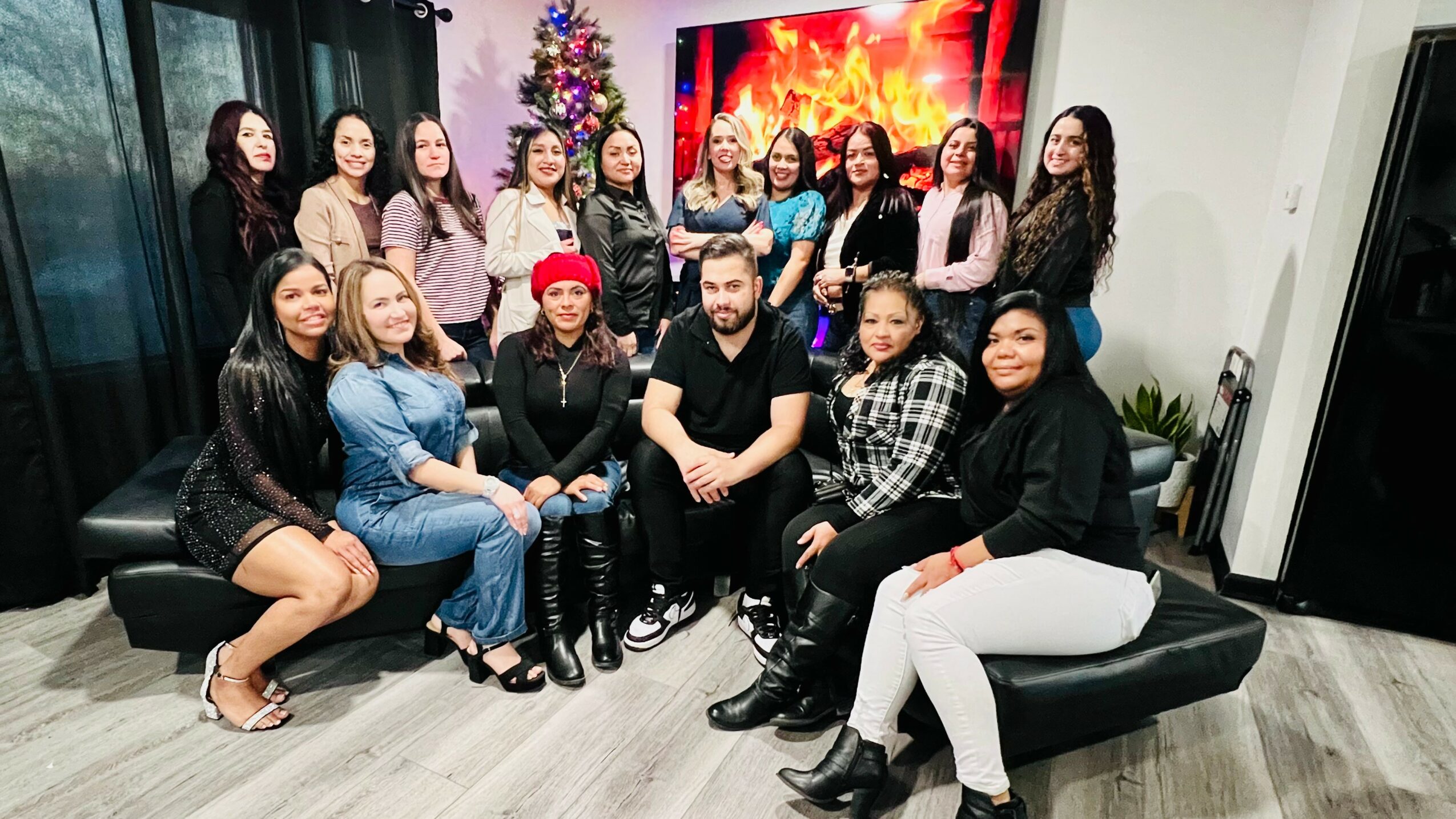 Group of 15 people gathered in a room with a Christmas tree and a large screen, some sitting and some standing.