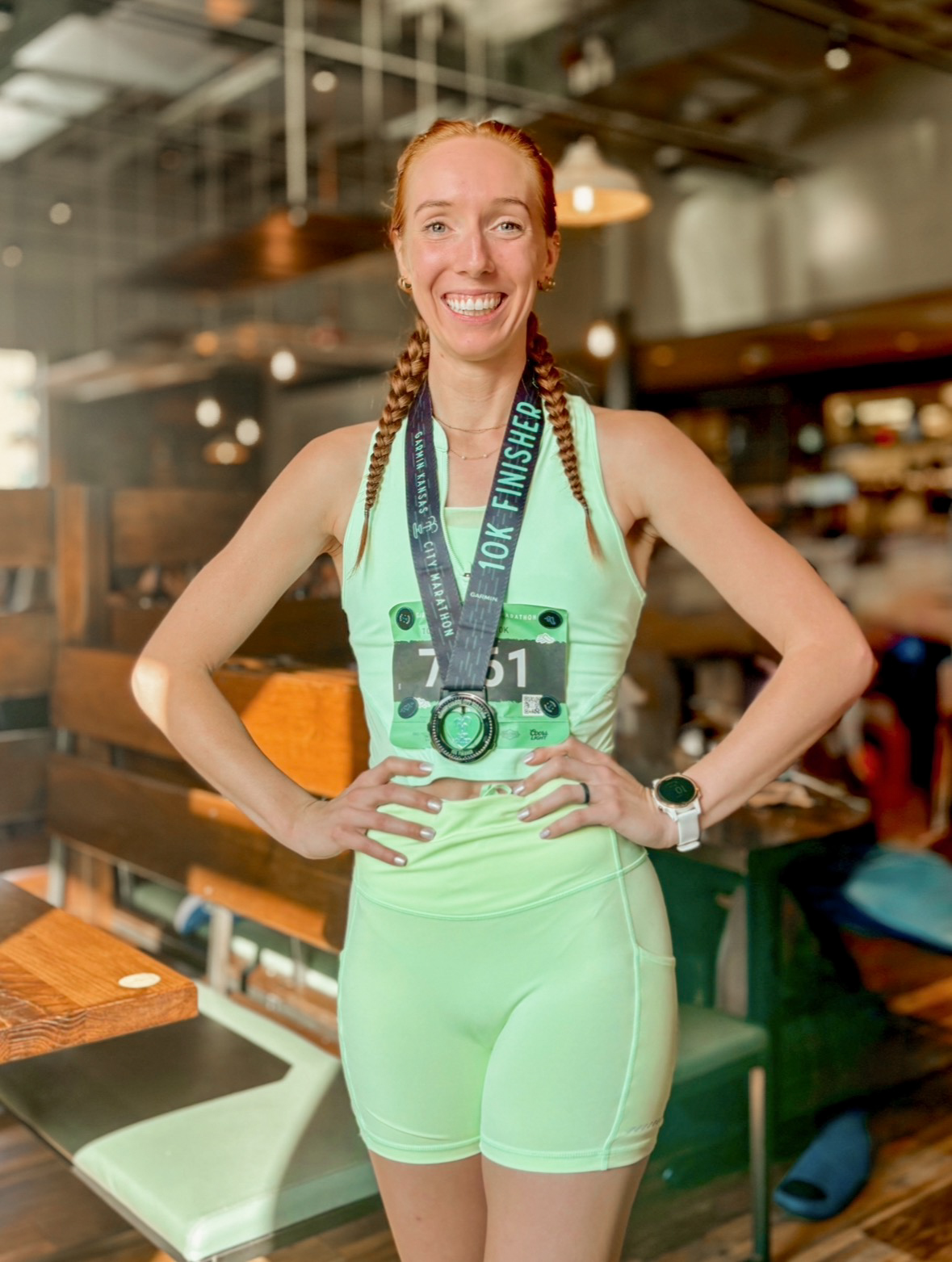 Smiling woman with braided hair wearing a medal and athletic outfit in a cafe or restaurant.