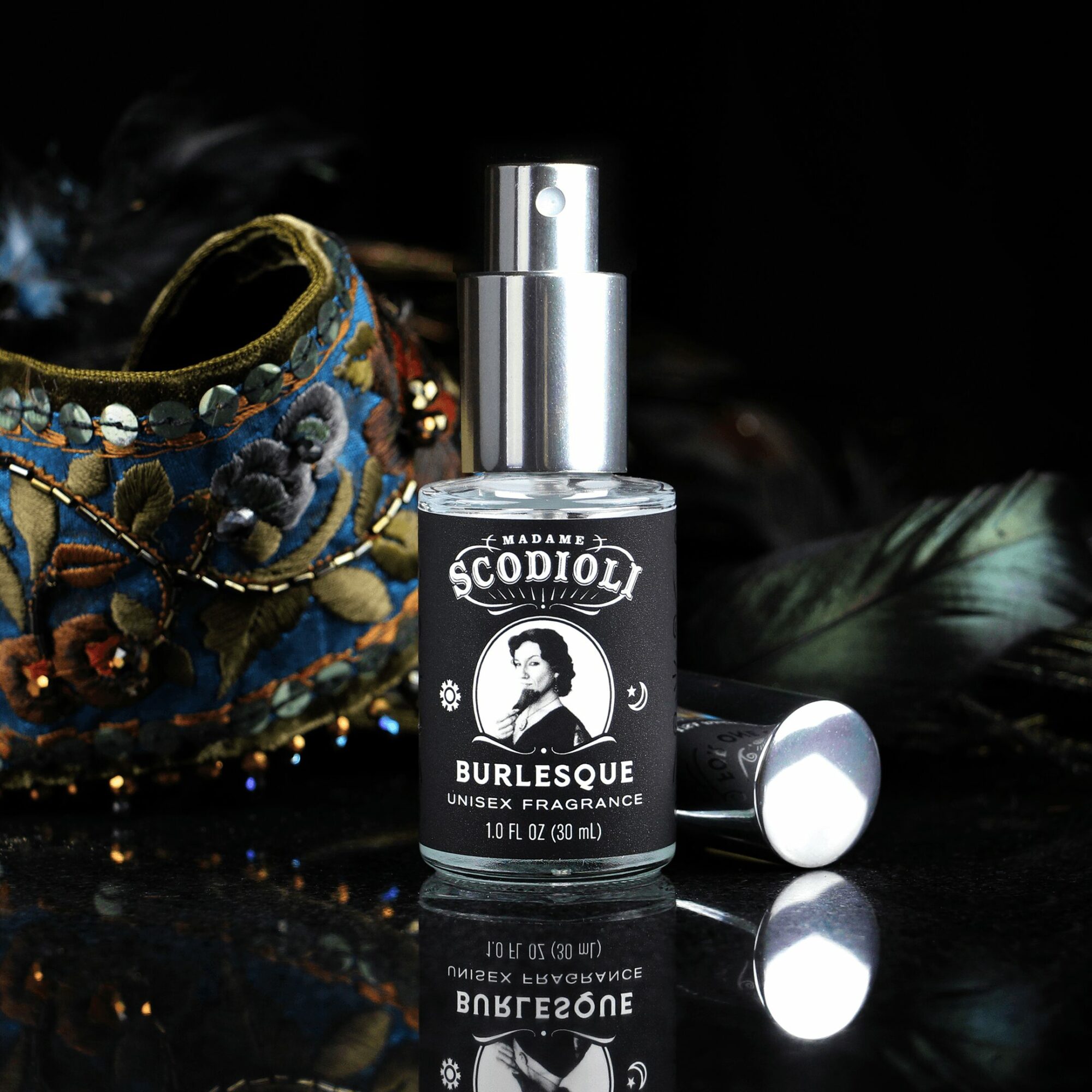A spray bottle labeled 'Burlesque' with a black and white design, placed on a dark surface with decorative items nearby.