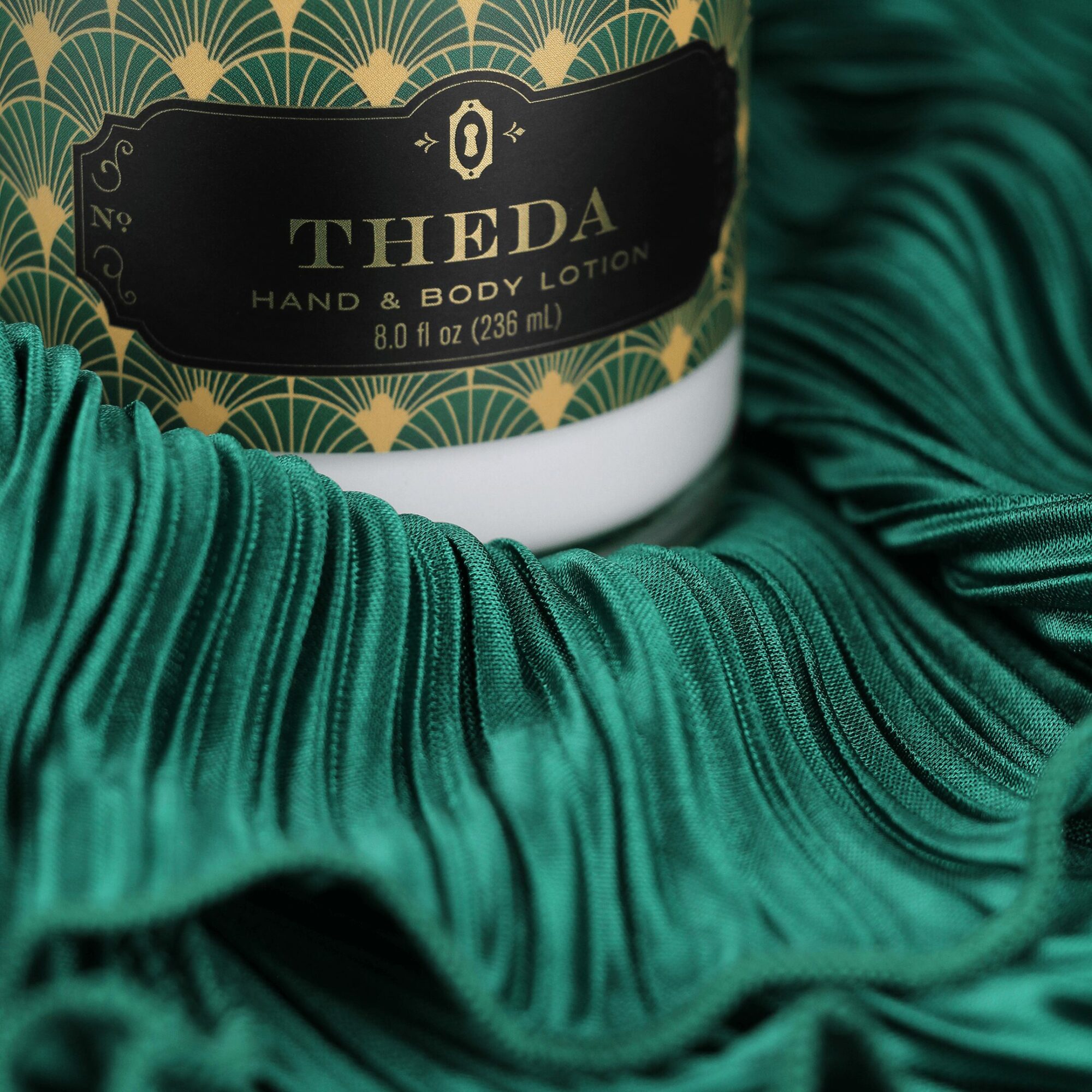 Close-up of a black and gold label on a container of hand and body lotion, surrounded by green fabric with pleats.