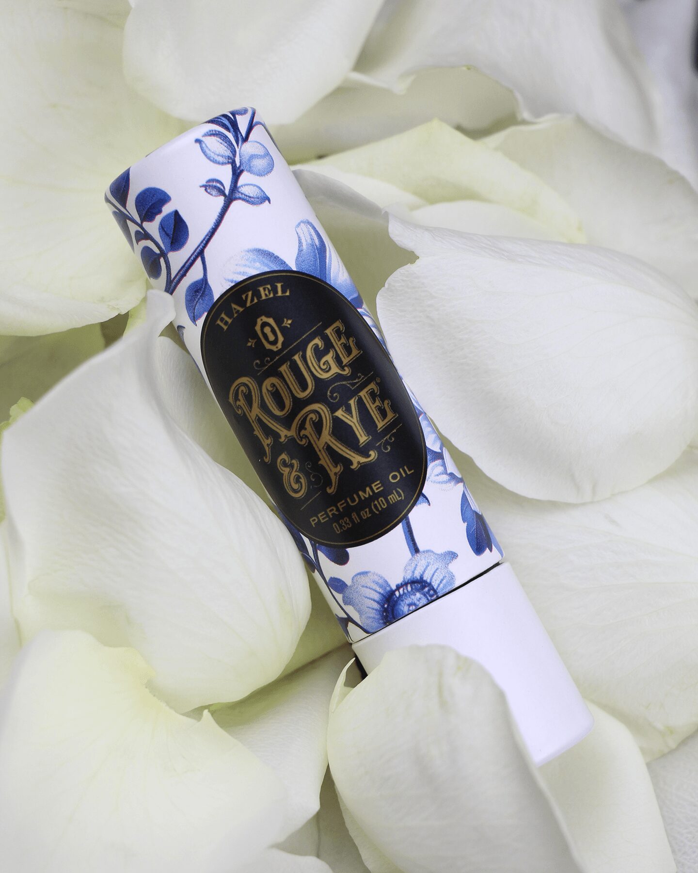 A lipstick tube with a blue floral design and gold lettering, surrounded by white rose petals.