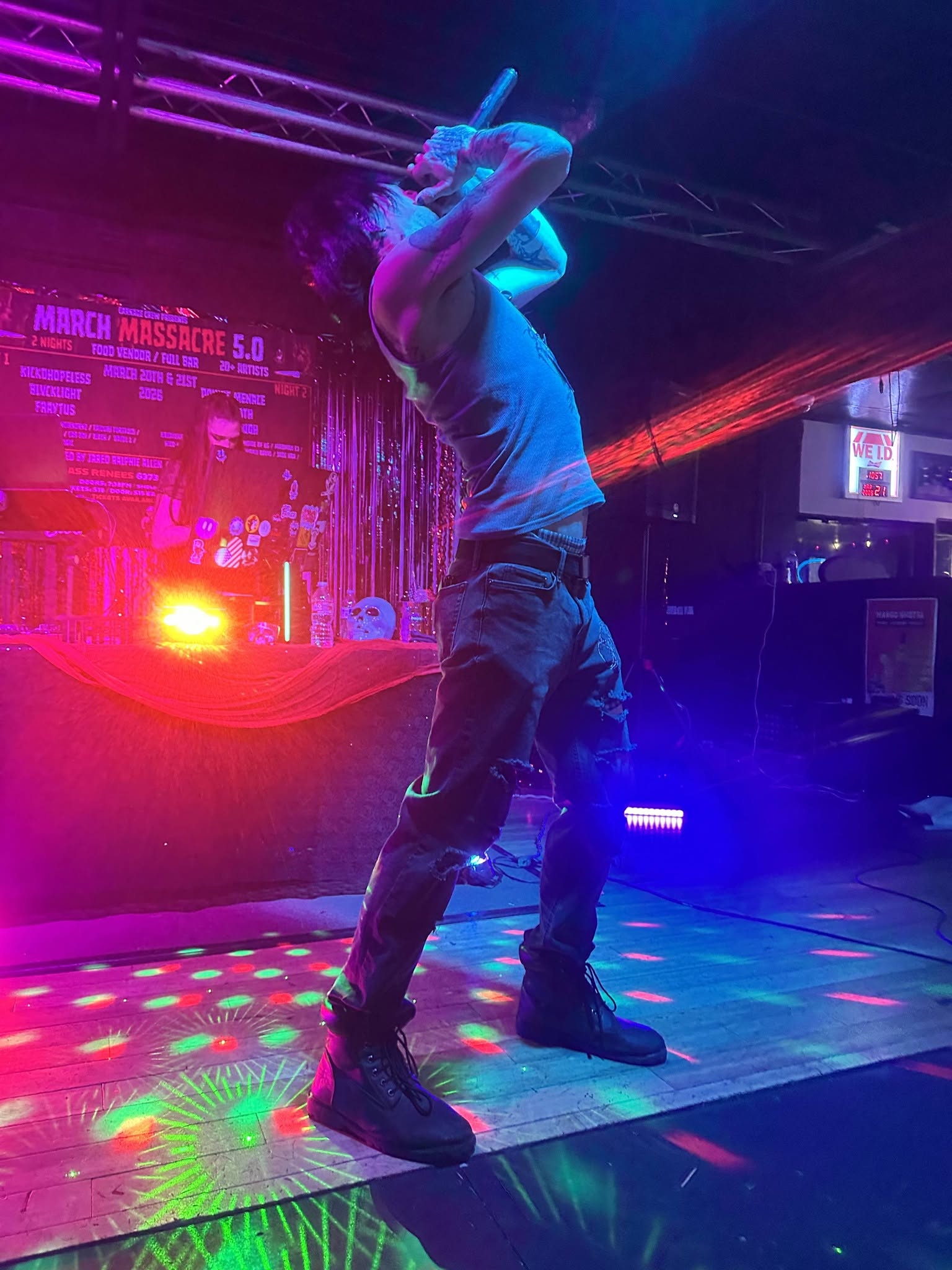 Person dancing on a colorful lit dance floor with stage lights and a DJ booth in the background.