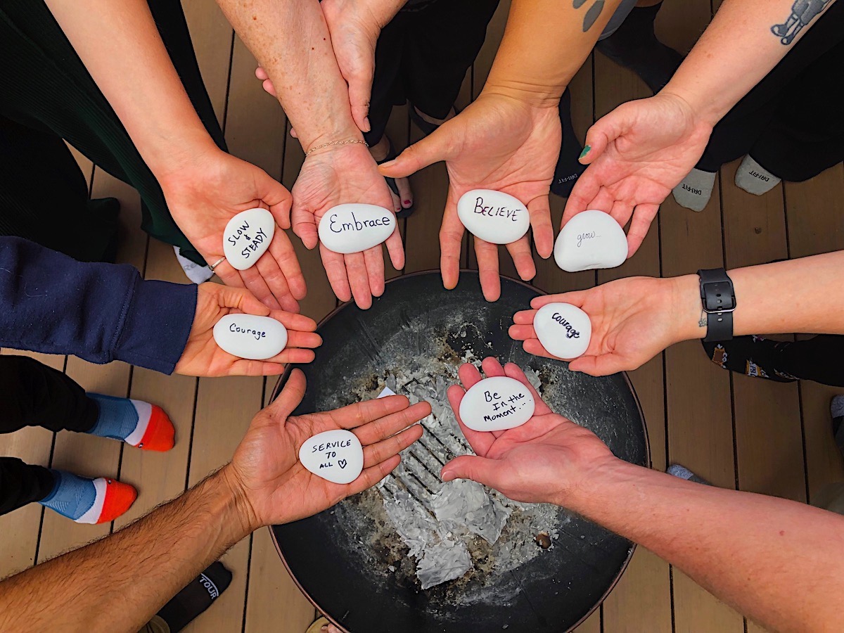 Multiple hands hold small paper notes with words like 'Embrace,' 'Dream,' and 'Change' around a black circular surface.