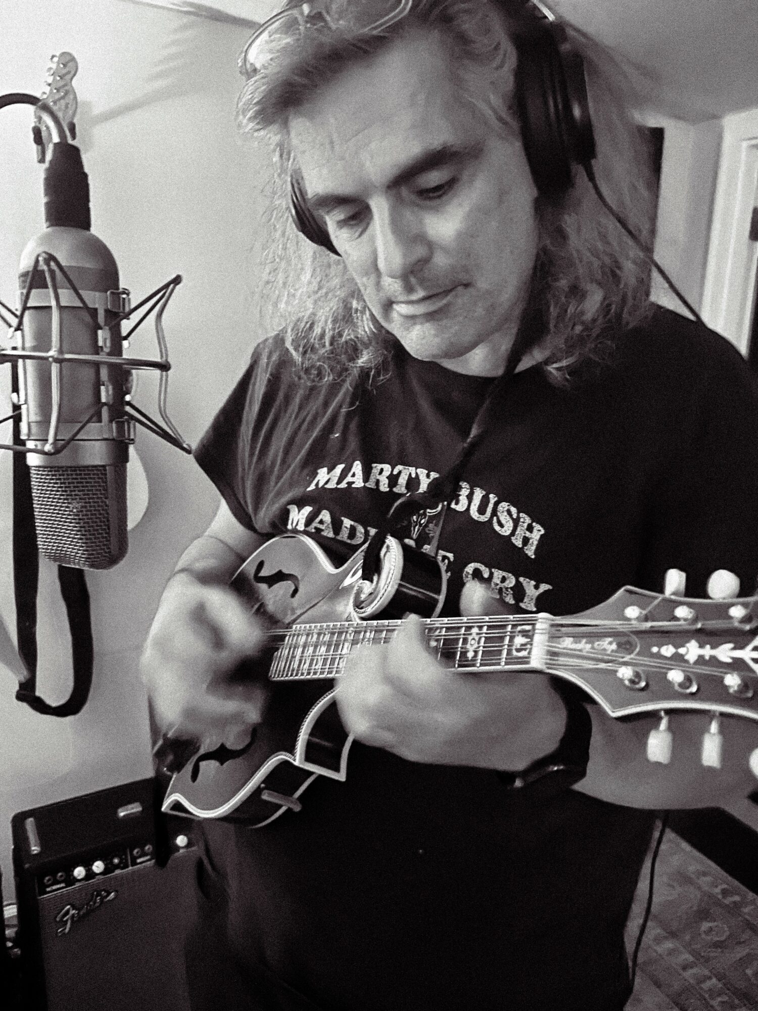 Person with long hair wearing headphones playing a small stringed instrument in a recording studio.