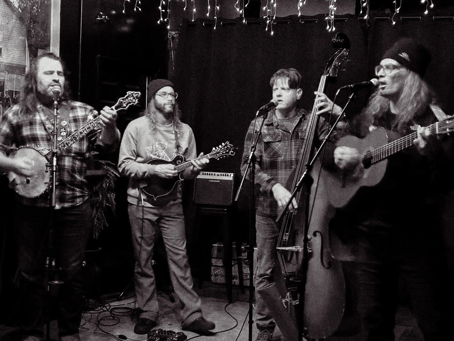 Four musicians perform on stage with guitars and a microphone, in a black-and-white setting.