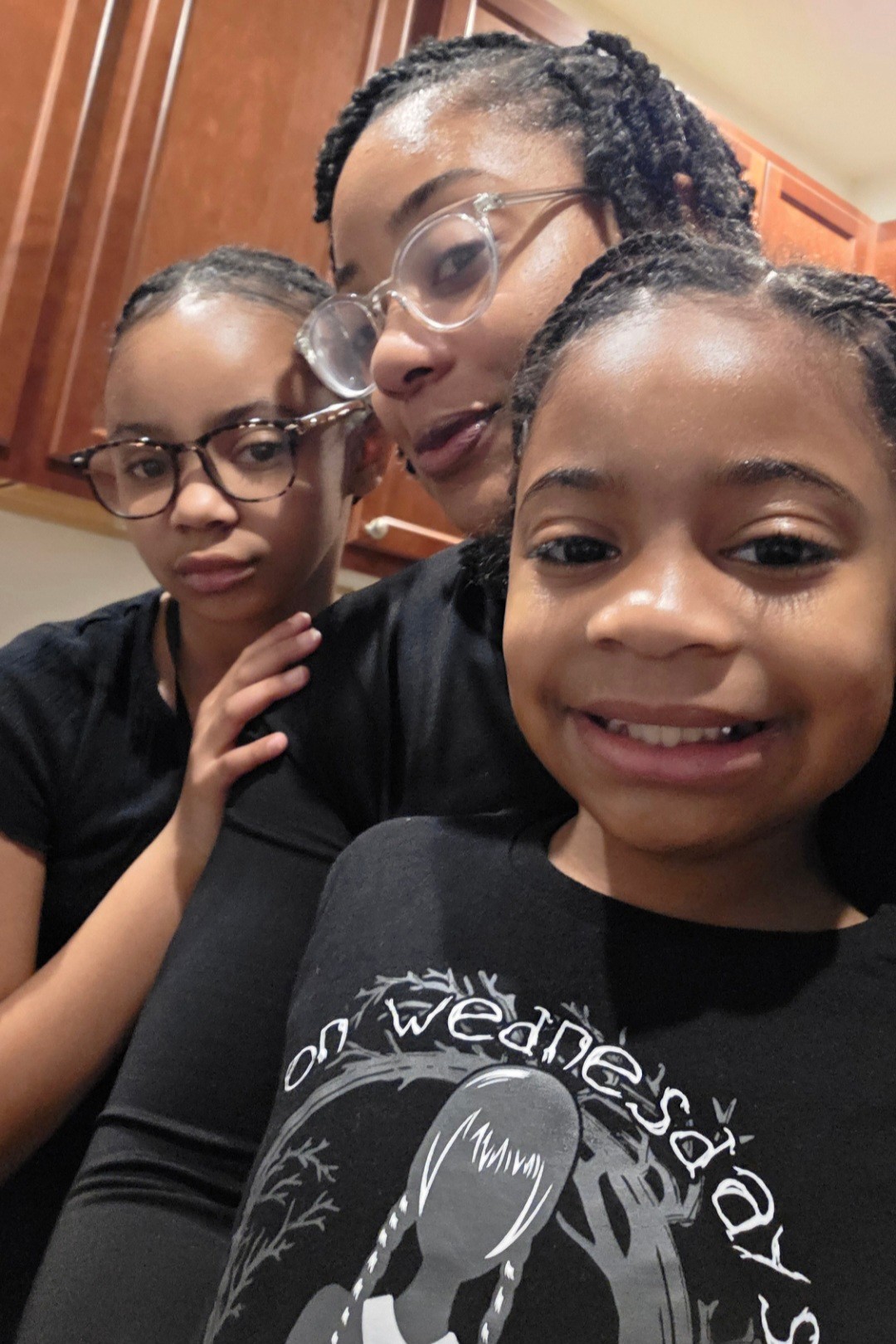 Three people, two children and an adult, close together indoors, smiling and looking at the camera.