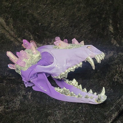 Purple and gold decorative skull with crystals and teeth, on dark background.