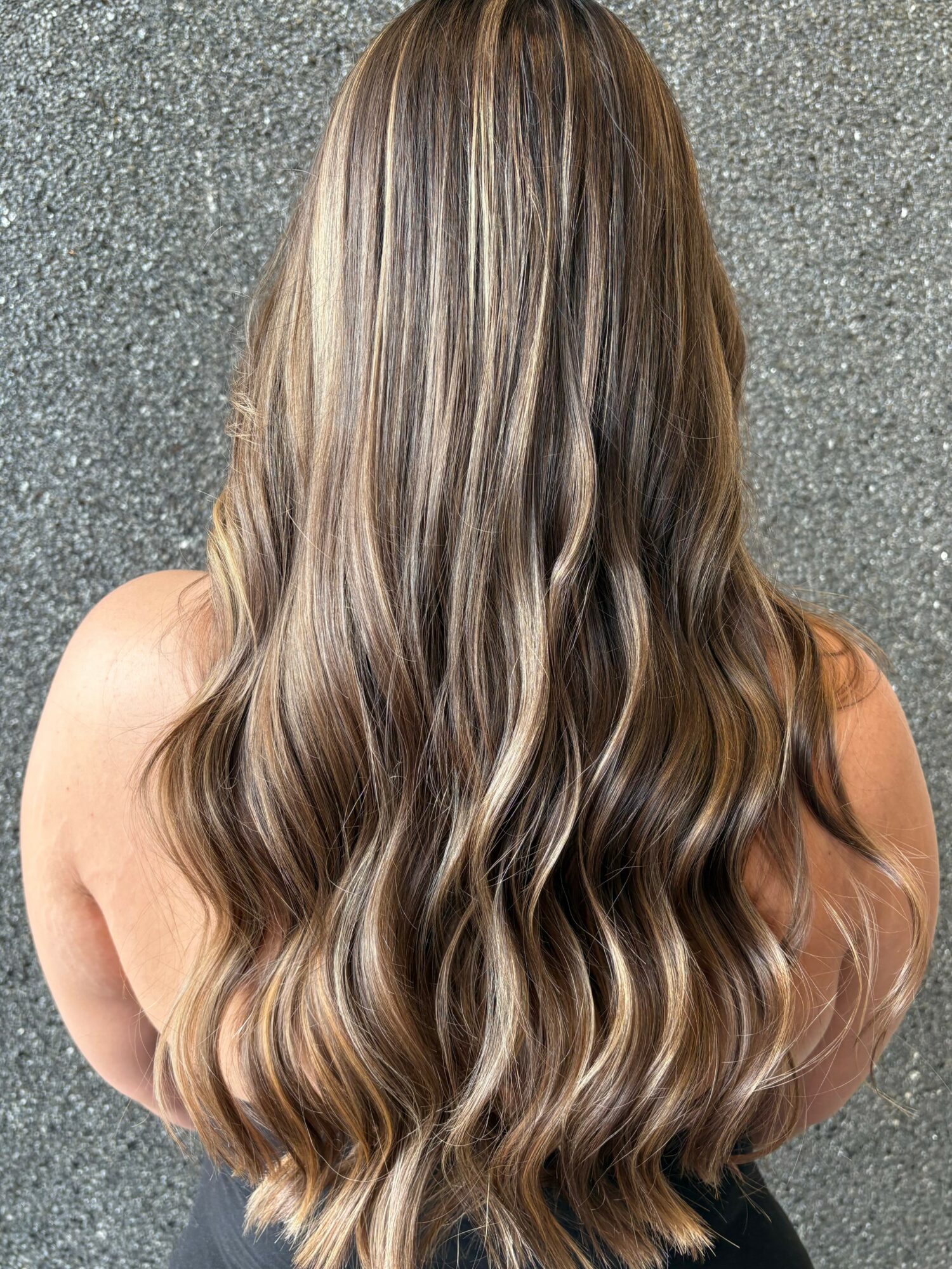Back view of long, wavy hair with blonde highlights against a textured gray background.
