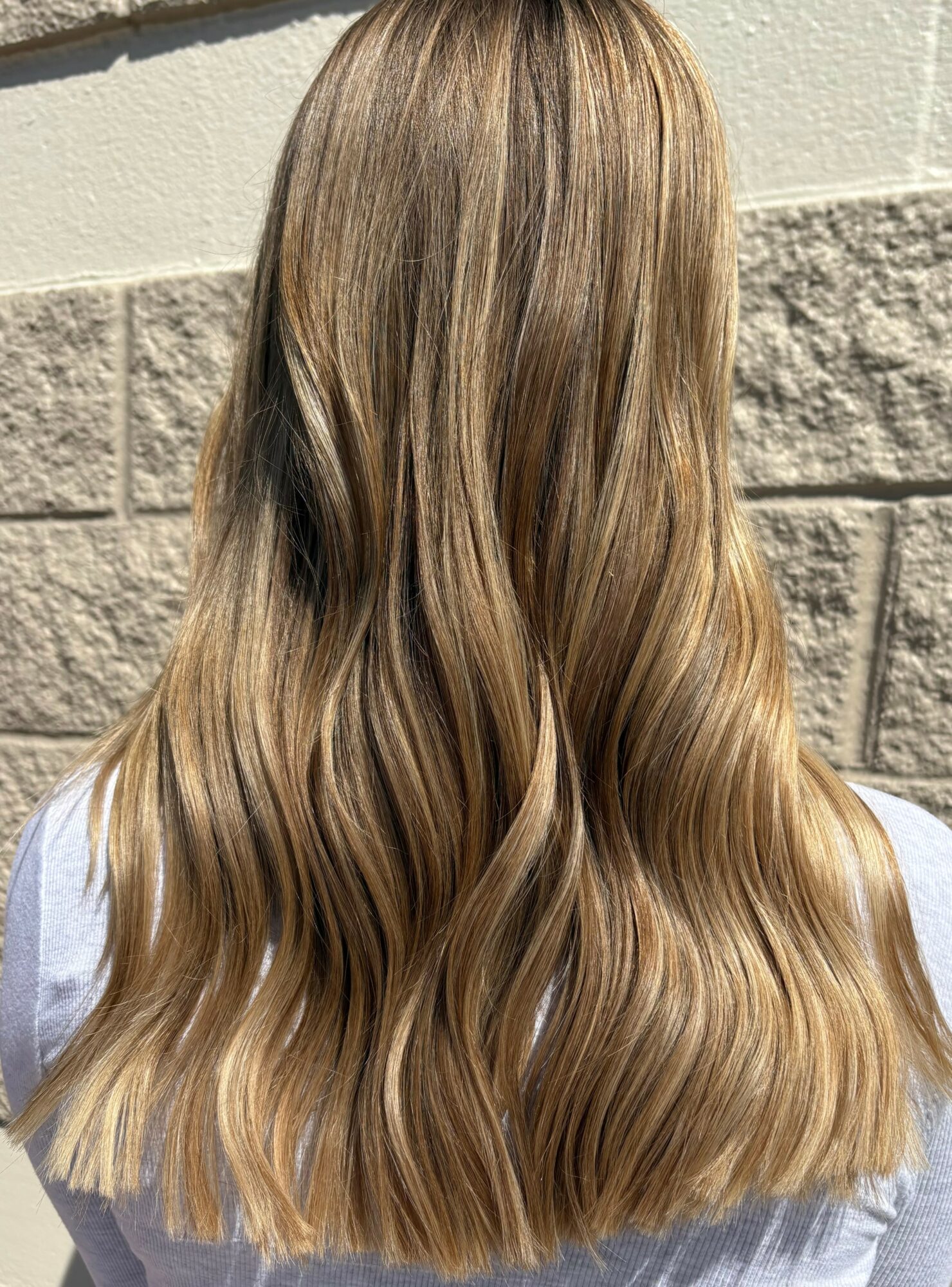 Back of a person with long, wavy, blonde hair standing outdoors against a brick wall.