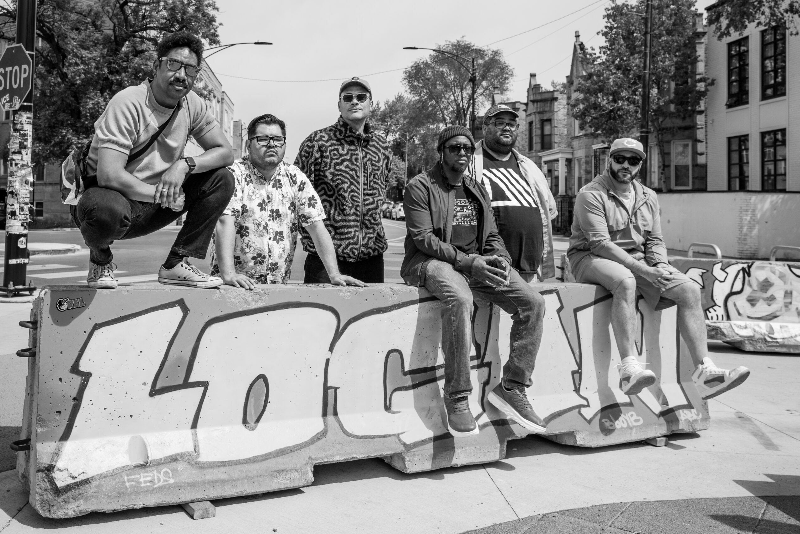 Group of six people sitting and standing on a large graffiti-covered block in an urban street scene, black and white.