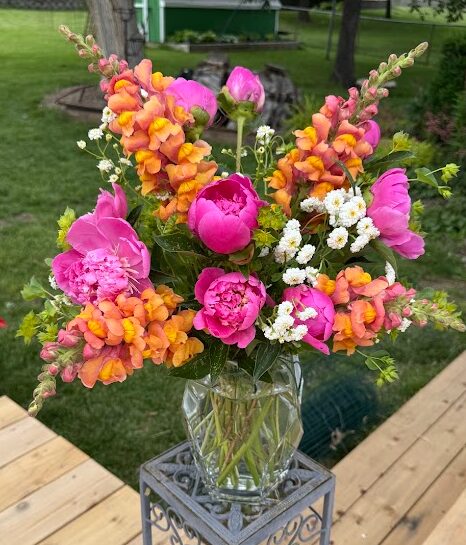 Colorful bouquet of pink, orange, and white flowers in a glass vase on a wooden table outdoors.