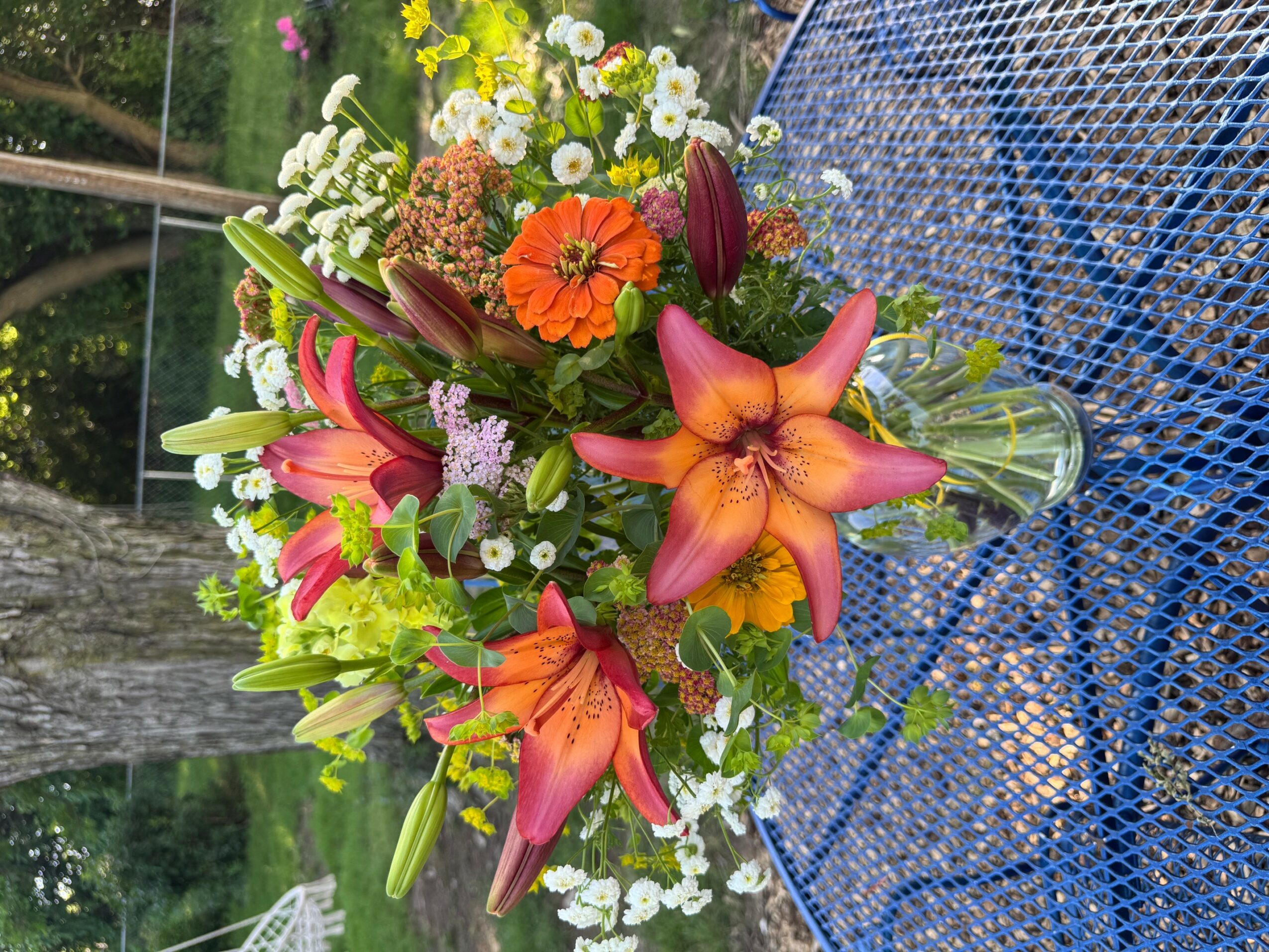Colorful flower bouquet with lilies, daisies, and other flowers on a blue surface, outdoors.