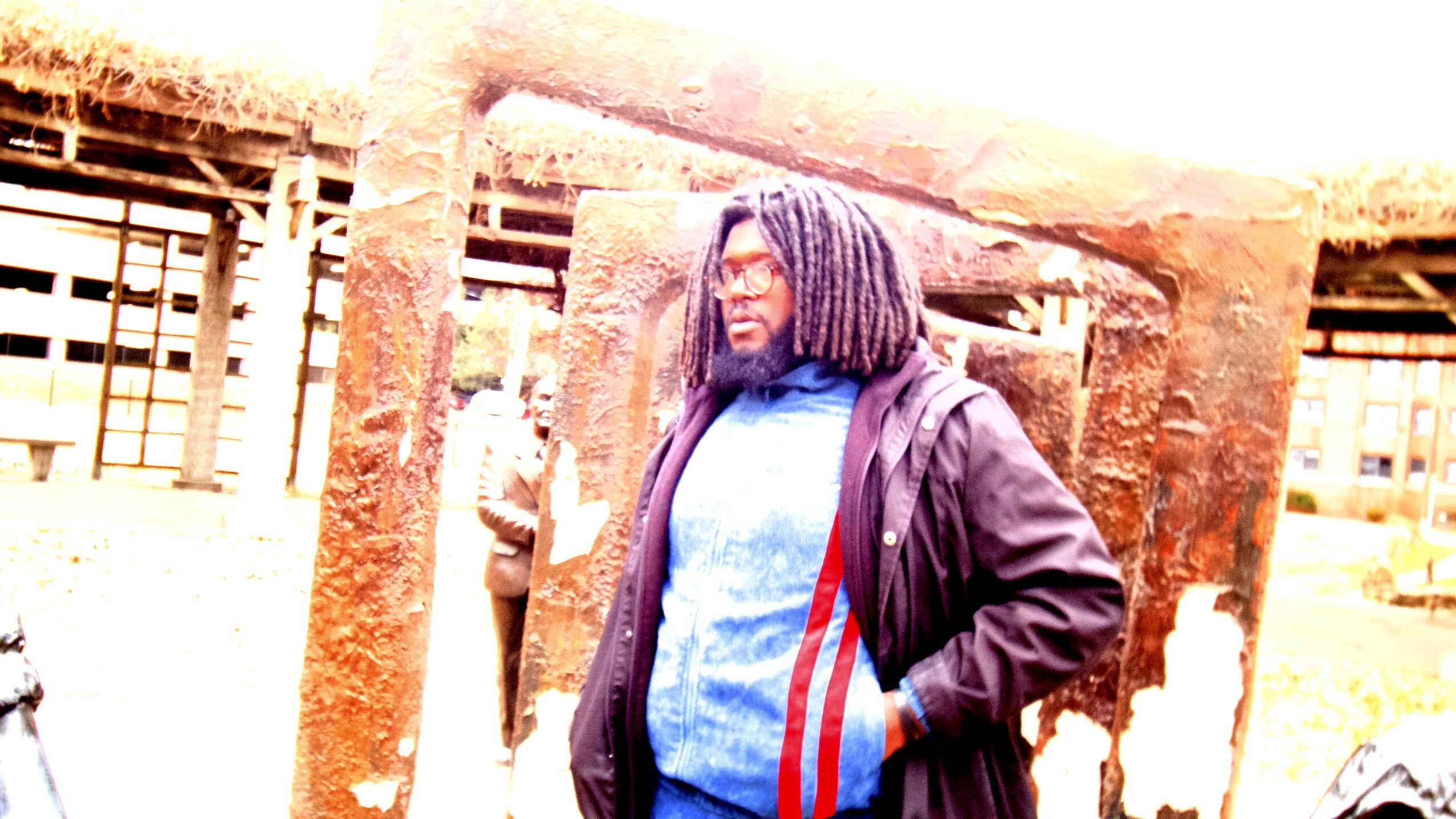 Person with long hair wearing a jacket, standing outdoors near wooden structures.