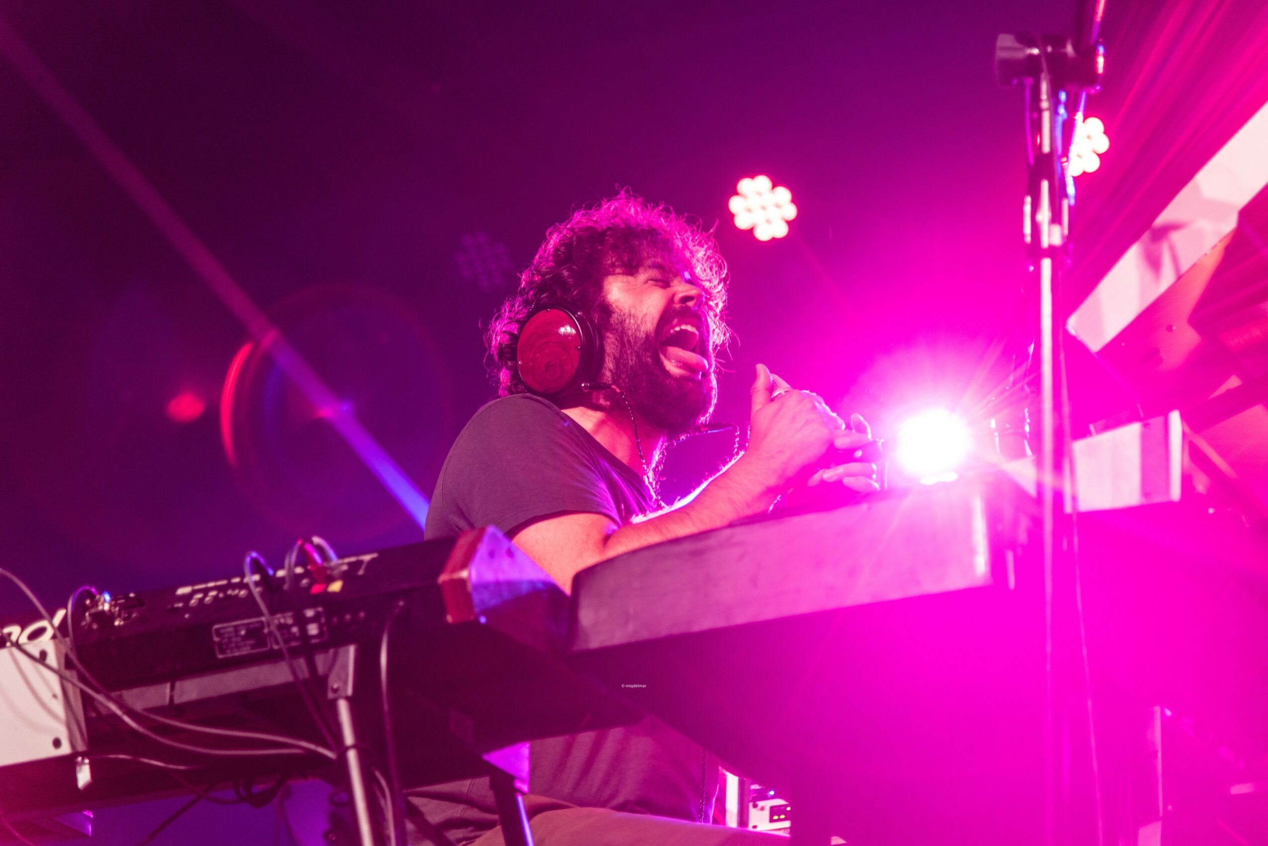 DJ with headphones operating equipment on stage, pink and purple lighting, bright light in background, dark surroundings