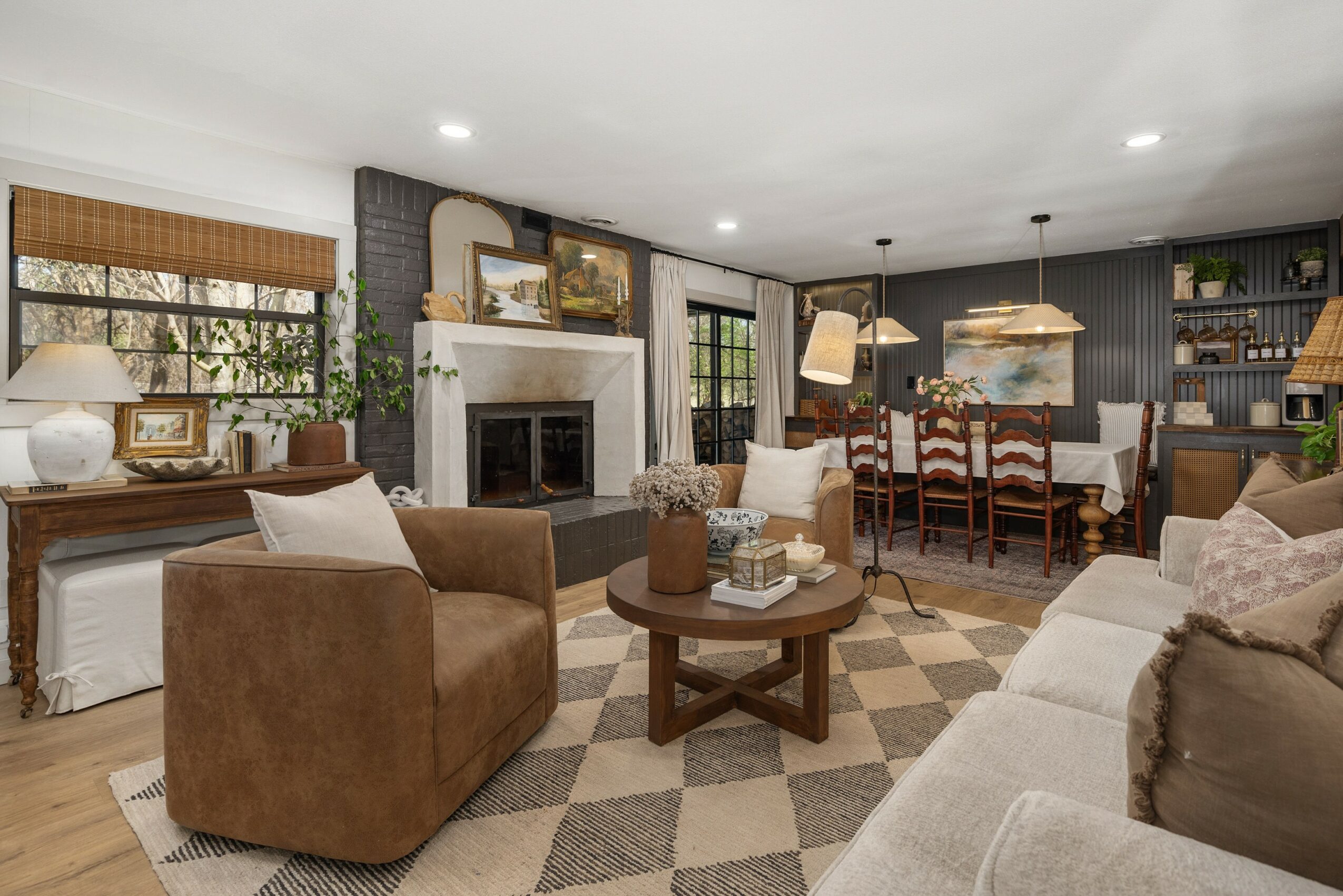 Living room with brown and beige sofas, a fireplace, and a dining area with wooden chairs and pendant lights.