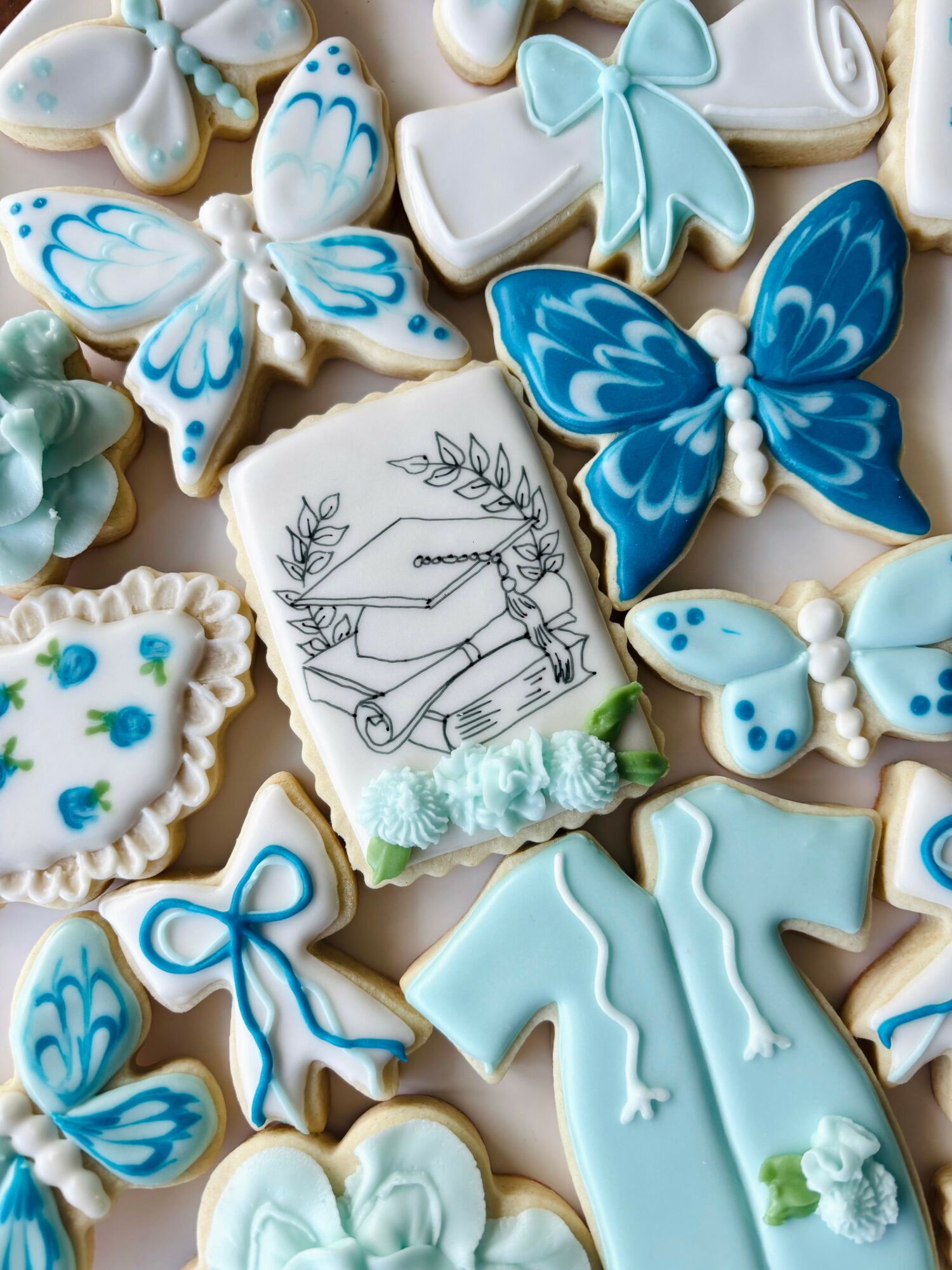 Collection of decorated cookies with butterflies, bows, and a book illustration, in pastel blue, white, and teal colors.
