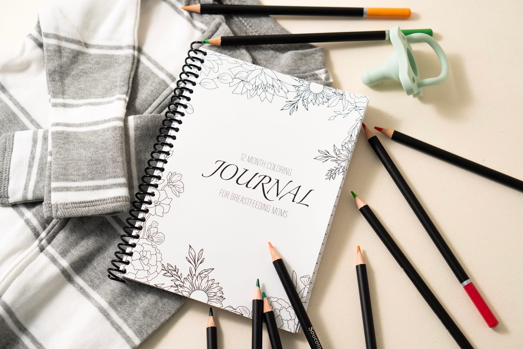 Open journal with floral cover, surrounded by pens, a cloth, and a pair of scissors on a light surface.