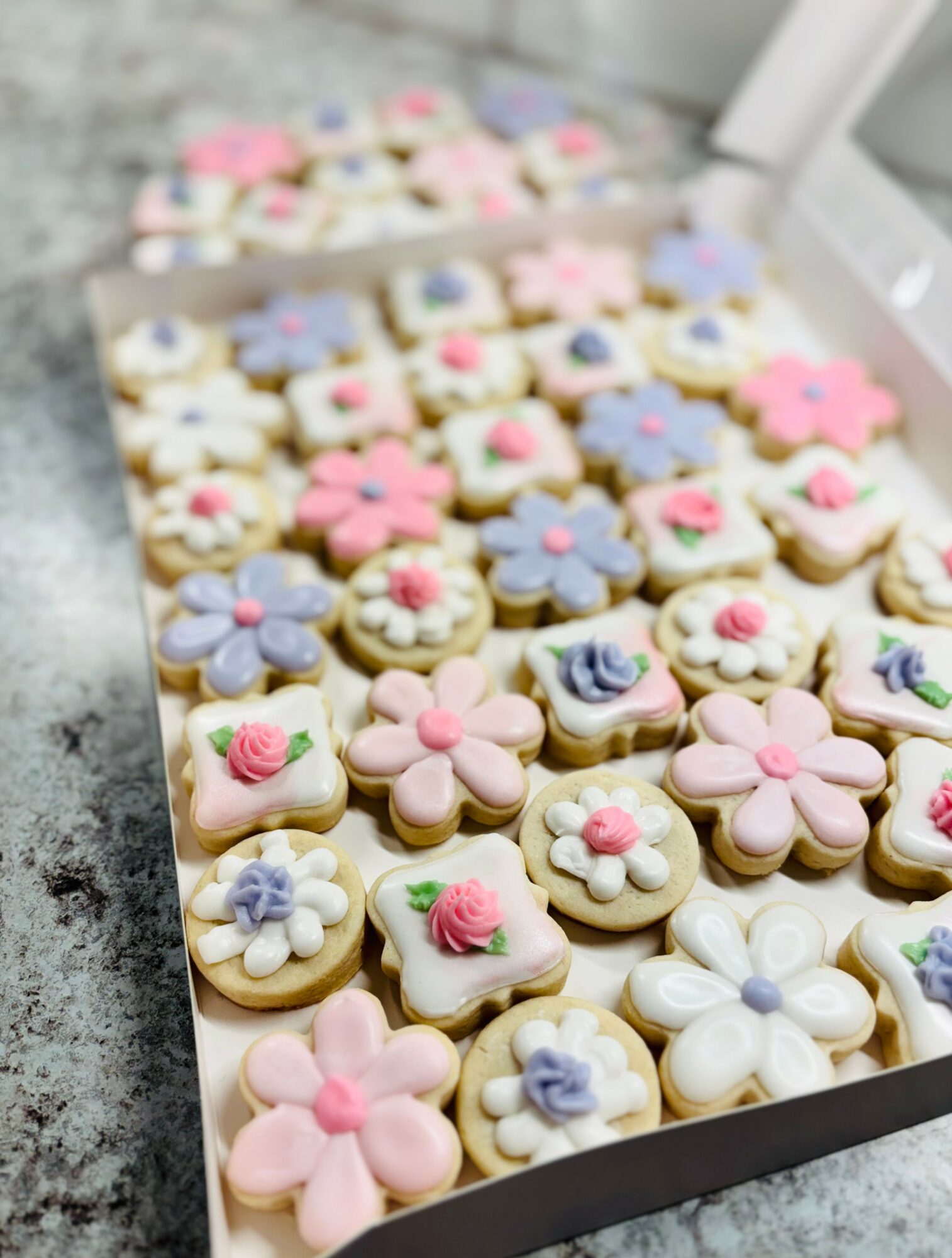 Assorted decorated cookies with floral and heart designs in a box on a countertop.