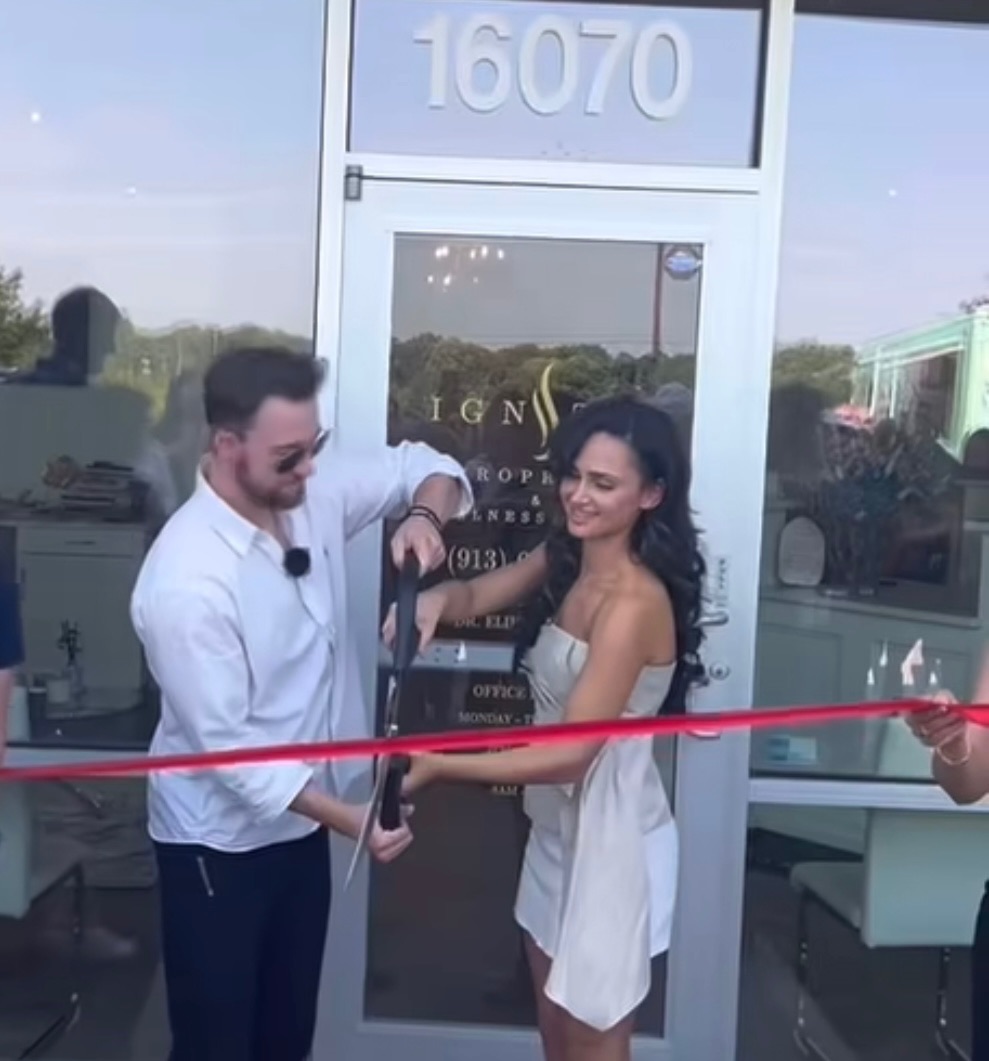 Man and woman at a ribbon-cutting event outside a building with the number 16070, smiling and holding scissors.