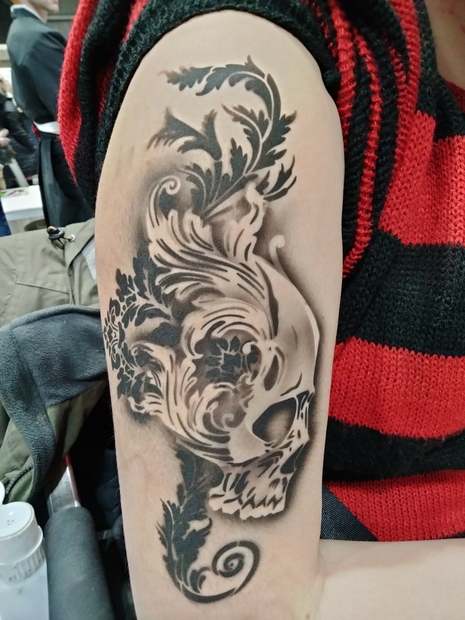 Tattoo of a stylized lion's face with flowing mane on person's upper arm, in black and gray ink.