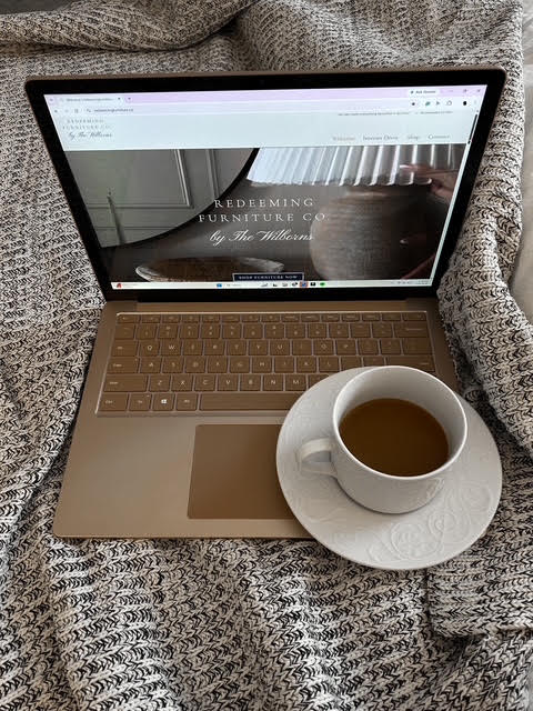Laptop with a cup of coffee on a saucer placed on a textured blanket.